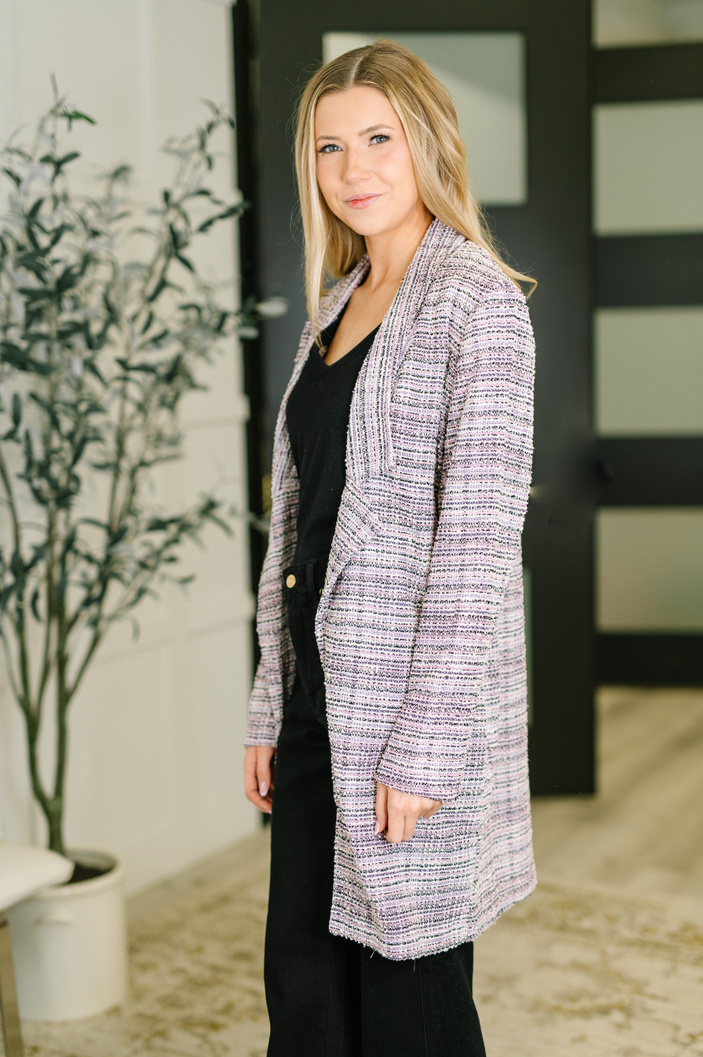 Woman wearing lavender ivory textured tweed midi blazer over black top and pants in modern indoor setting