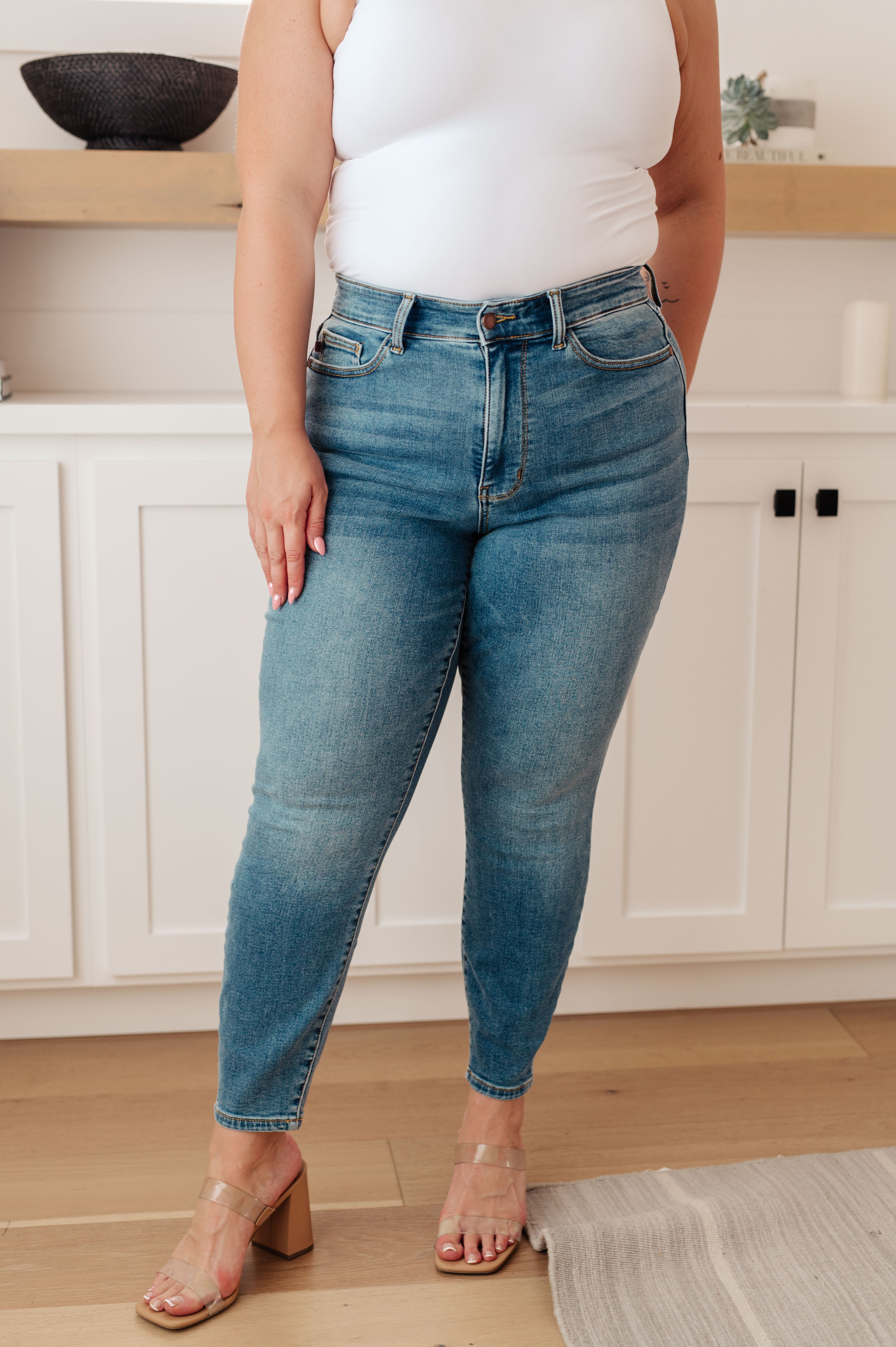 Plus size model wearing mid-blue high rise thermal skinny jeans with clear block heel sandals indoors