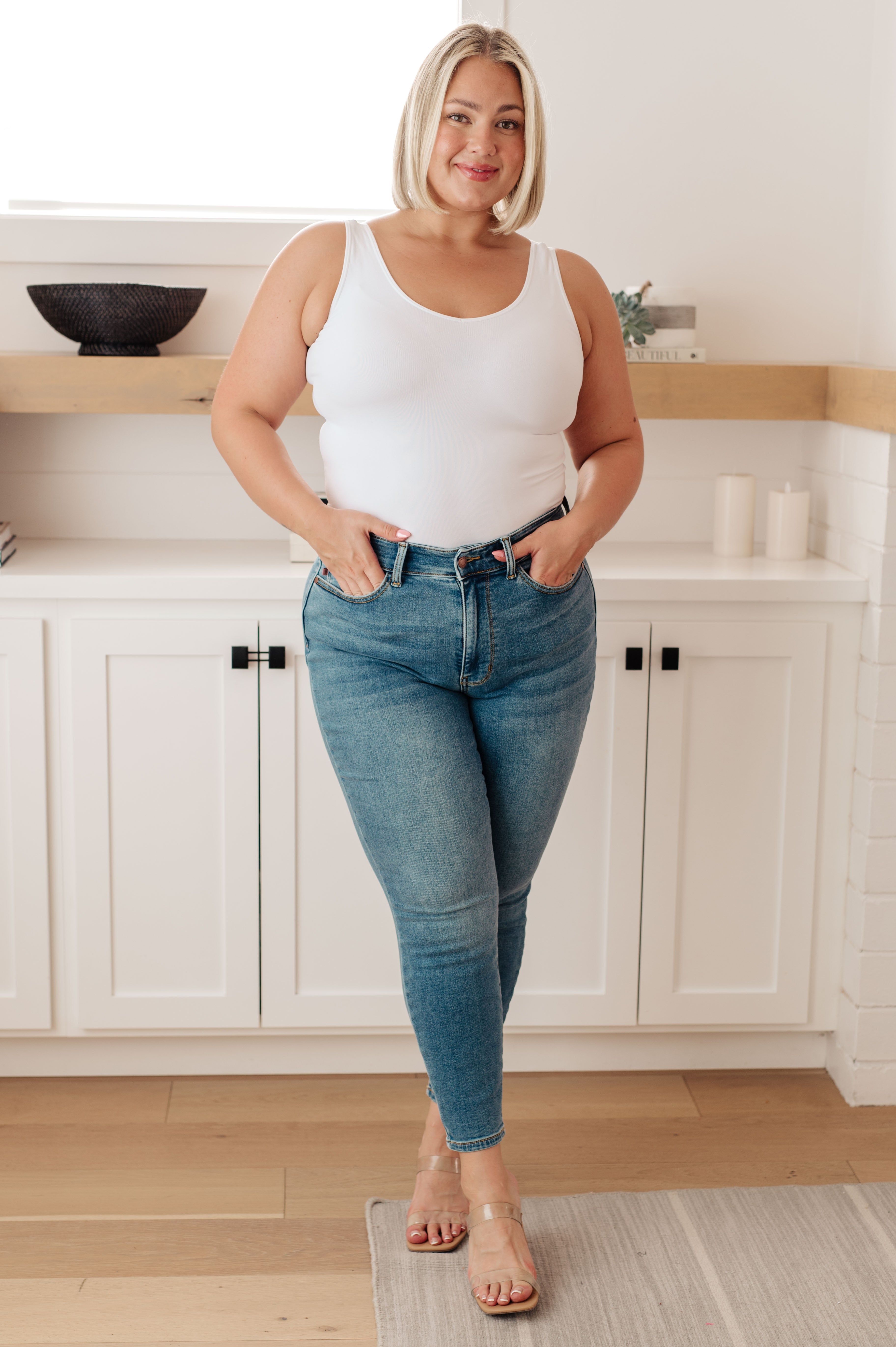 Plus size woman wearing mid-wash Bryant high rise thermal skinny jeans with clear strap sandals indoors