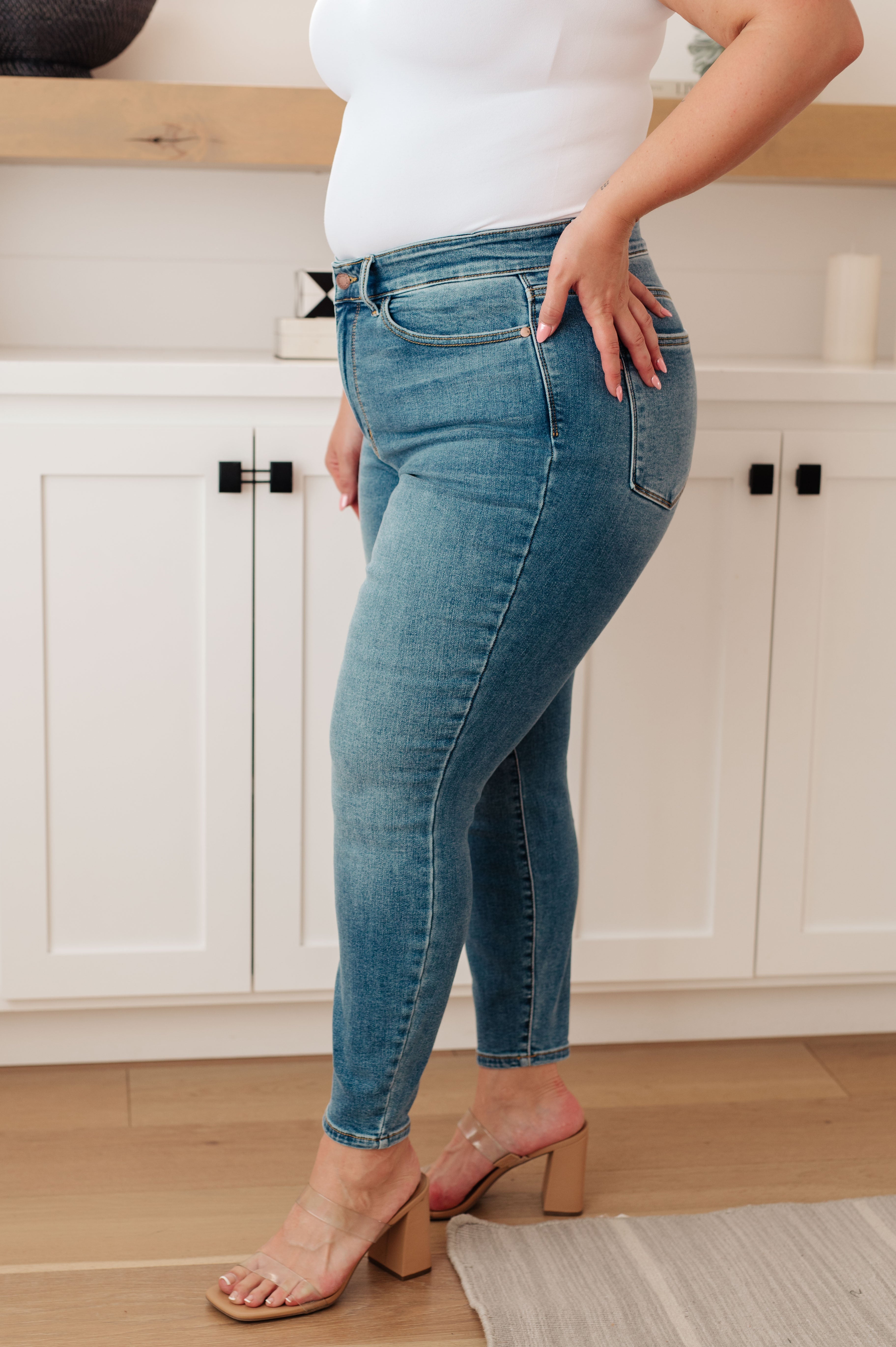 Woman wearing light wash Bryant high rise thermal skinny jeans with clear block heel sandals indoors