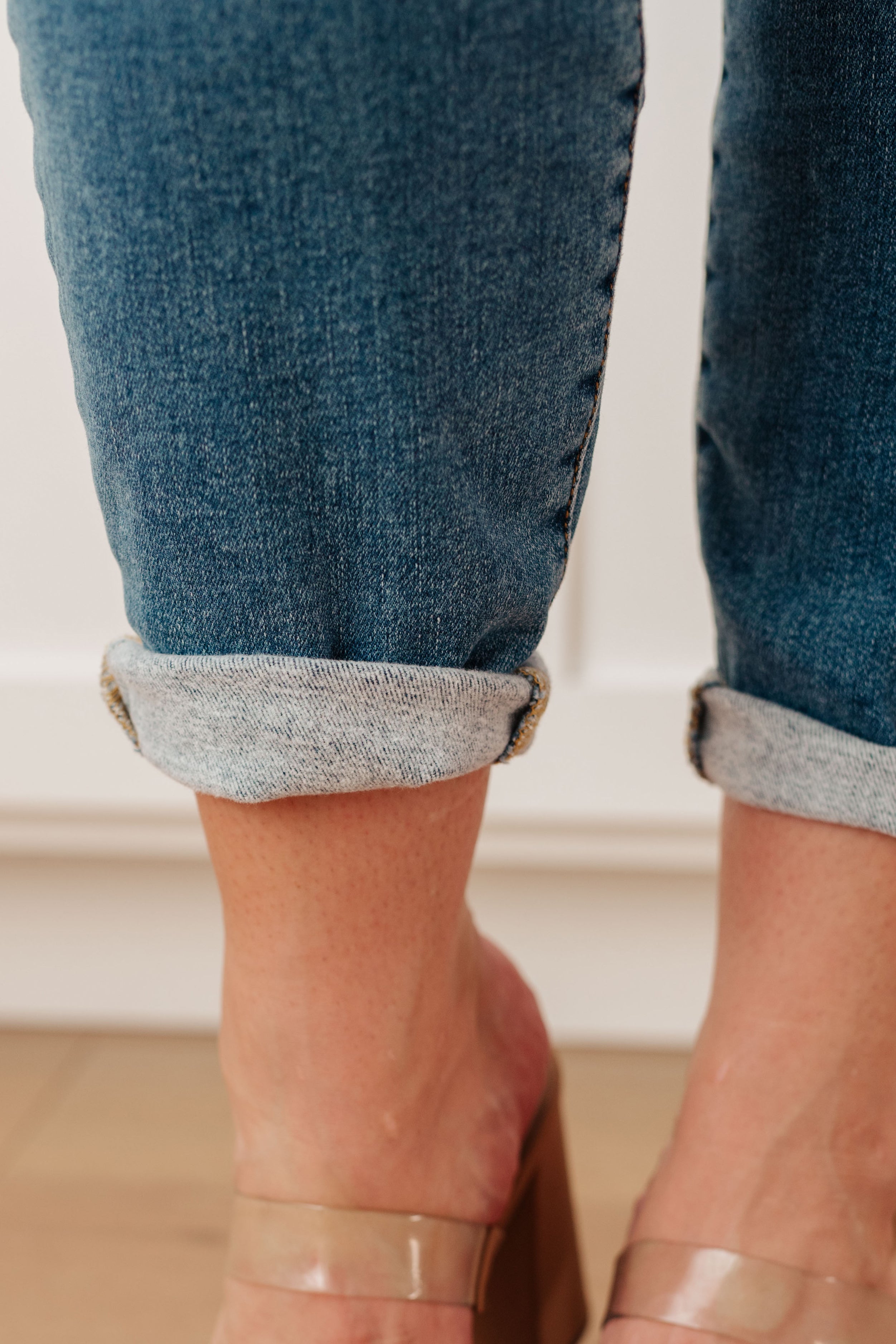 Close-up of rolled cuff on blue high rise thermal skinny jeans worn with clear block heel sandals