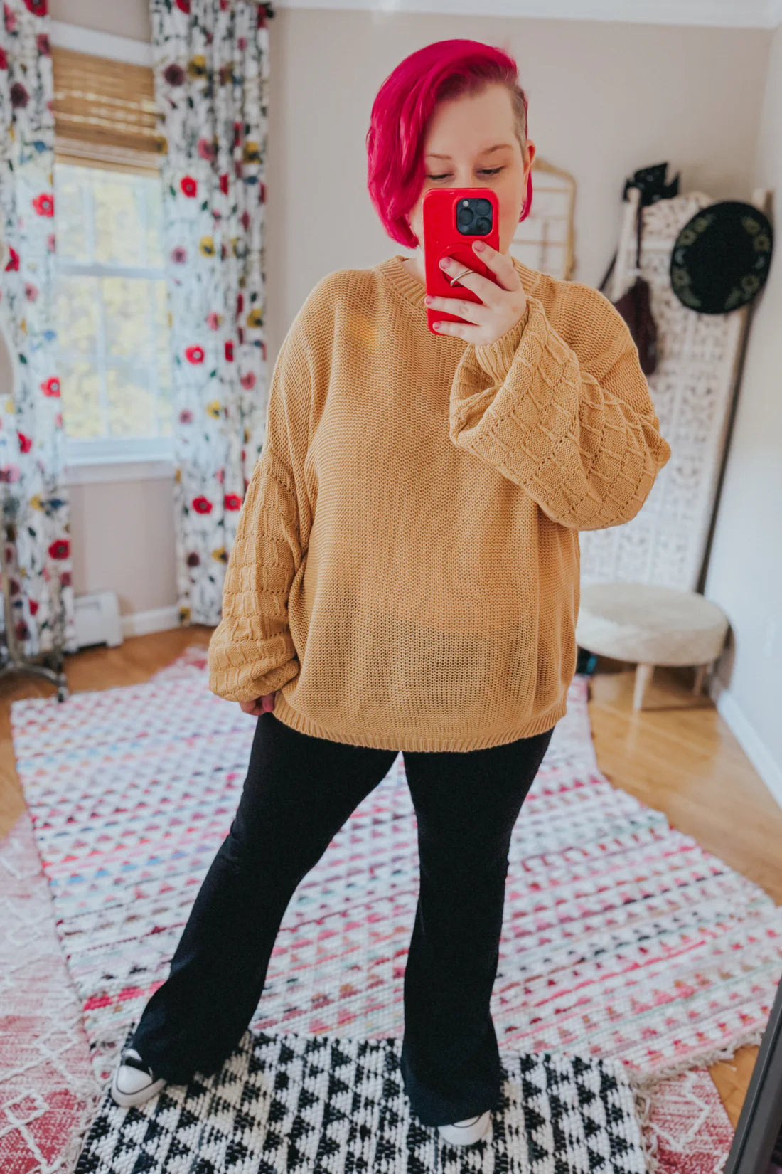 Woman wearing wheat-colored bubble sleeve sweater paired with black pants and standing in a bright room with patterned rugs
