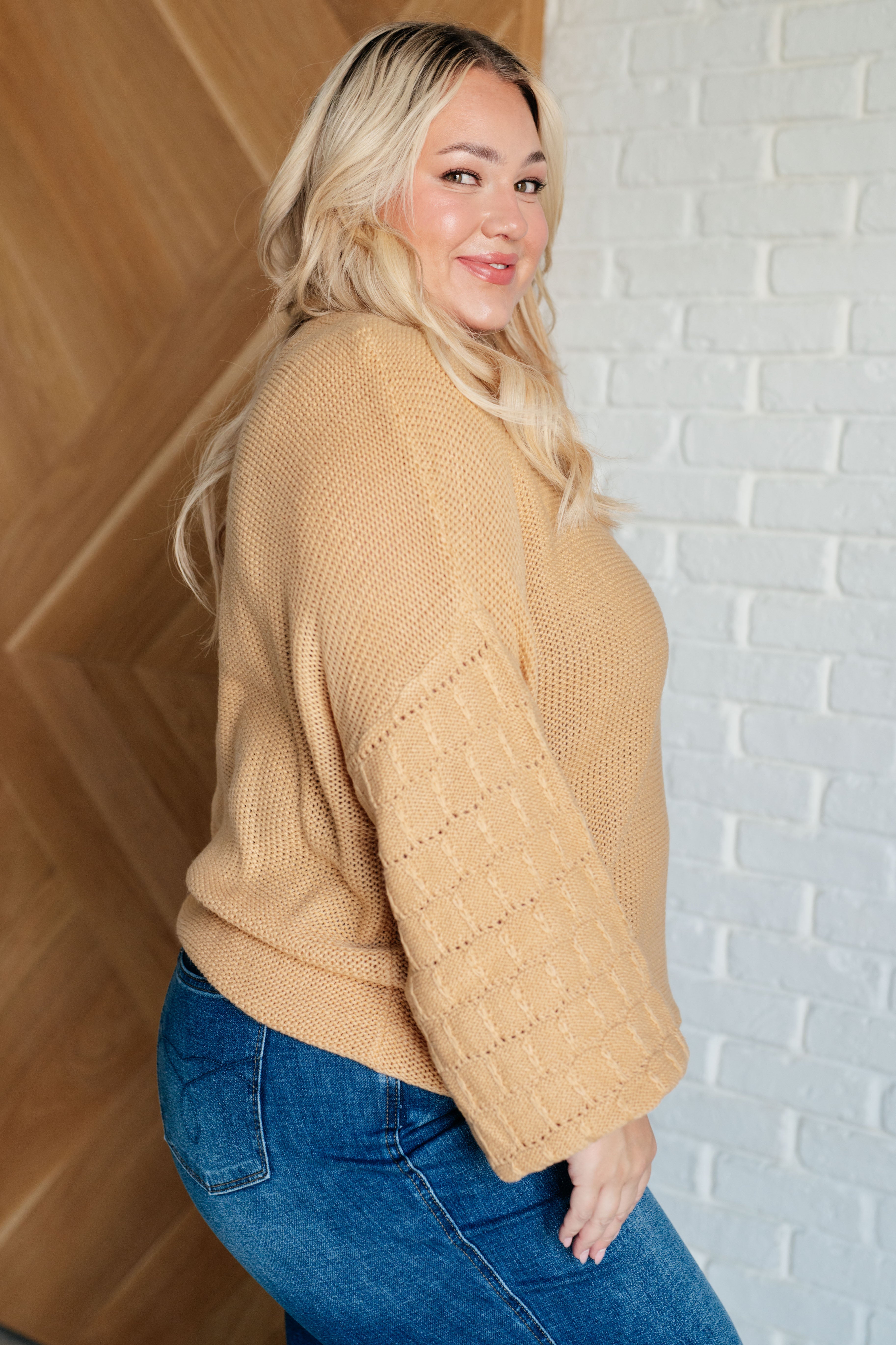 Profile of woman smiling while wearing a wheat-colored sweater with textured balloon sleeves and blue jeans indoors