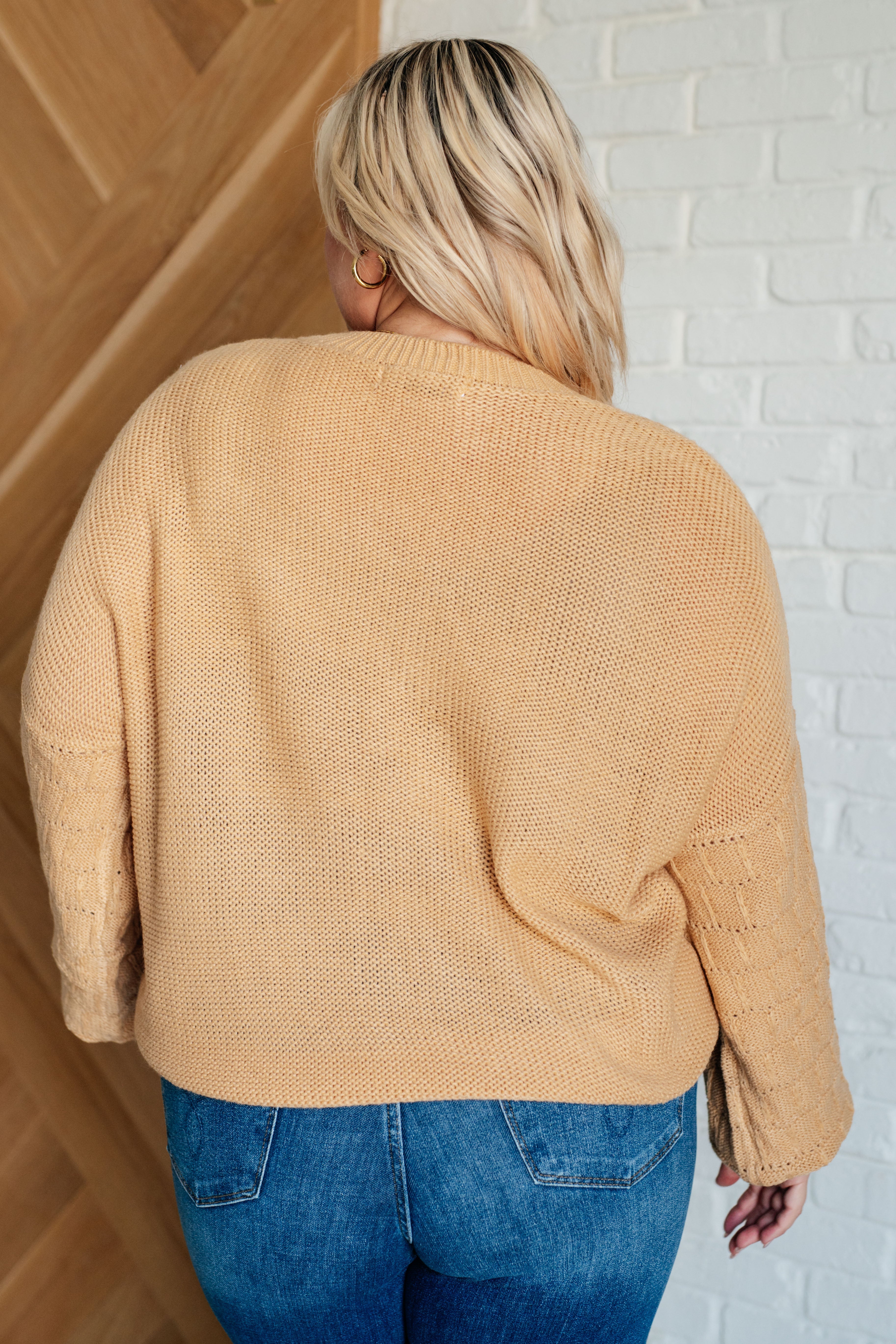 Back view of person wearing wheat-colored knit bubble sleeve sweater with textured sleeves and blue jeans indoors