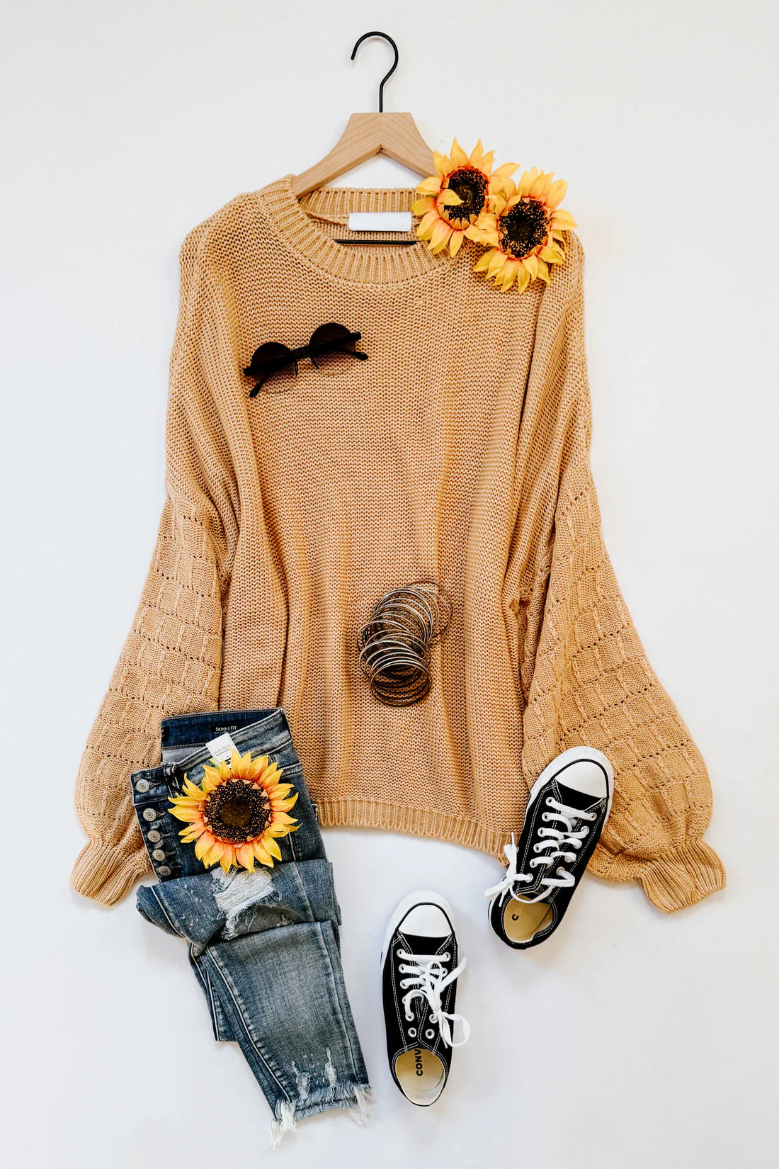 Wheat-colored bubble sleeve sweater styled with distressed jeans, black sneakers, sunflower accents, and sunglasses on hanger