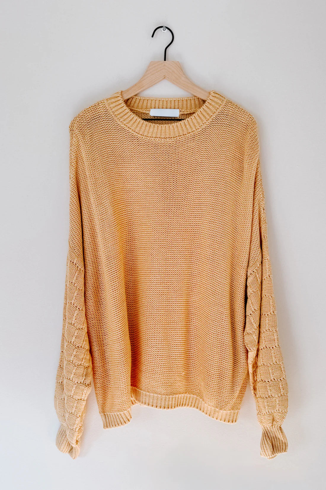 Wheat-colored textured knit sweater with bubble sleeves hanging on wooden hanger against white wall