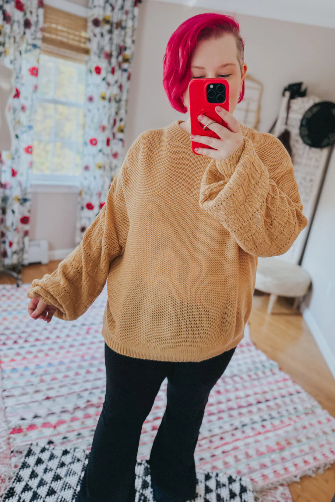 Woman taking selfie wearing wheat-colored bubble sleeve sweater with textured knit and black pants in cozy room