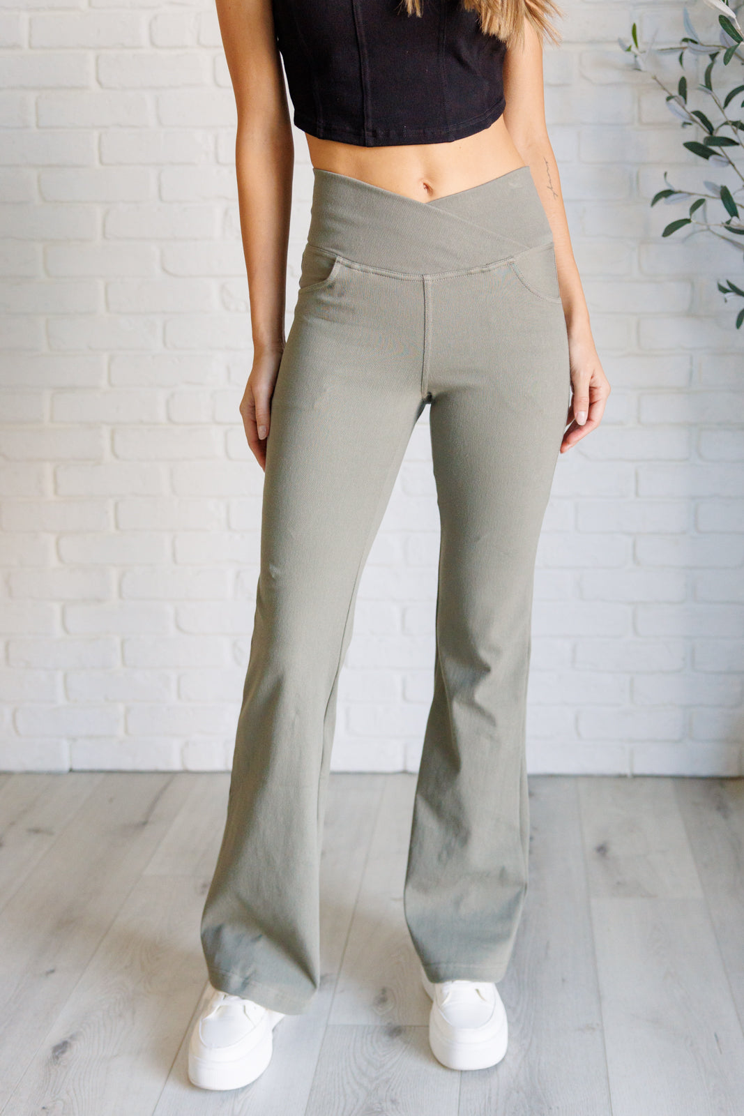 Woman wearing dusty olive twill pants with flared legs and crossover waist standing on light wood floor indoors