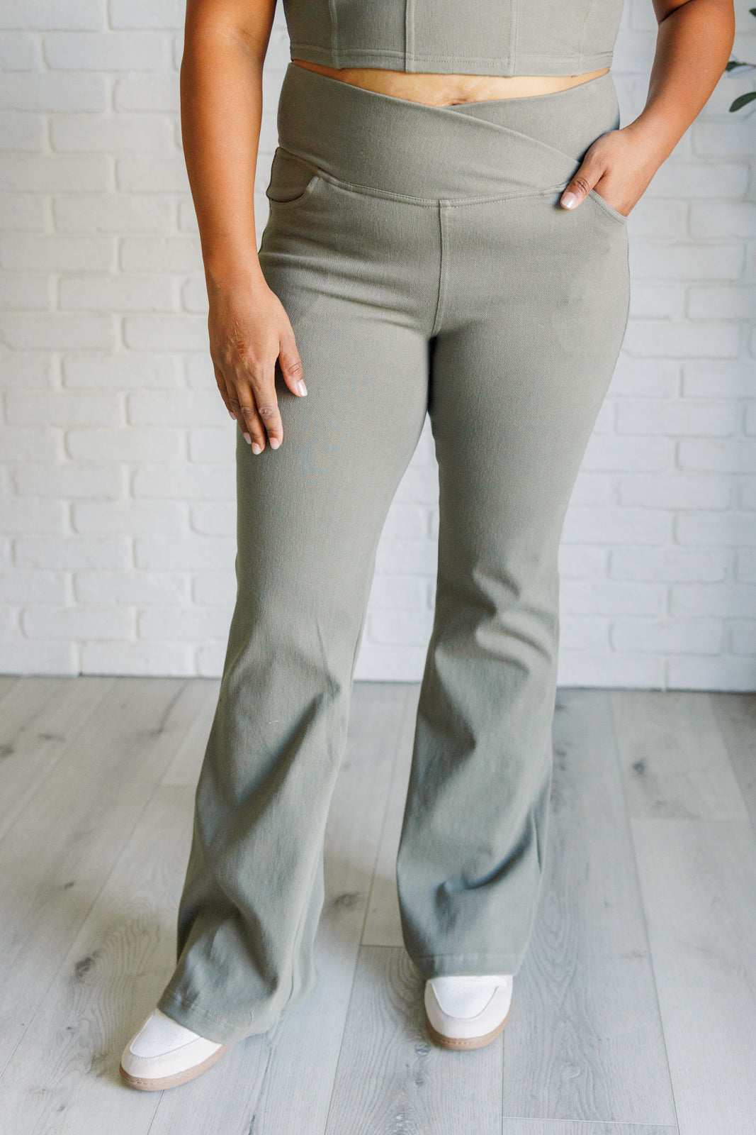 Close-up of person wearing dusty olive crossover waist twill pants with flared legs and front pockets indoors