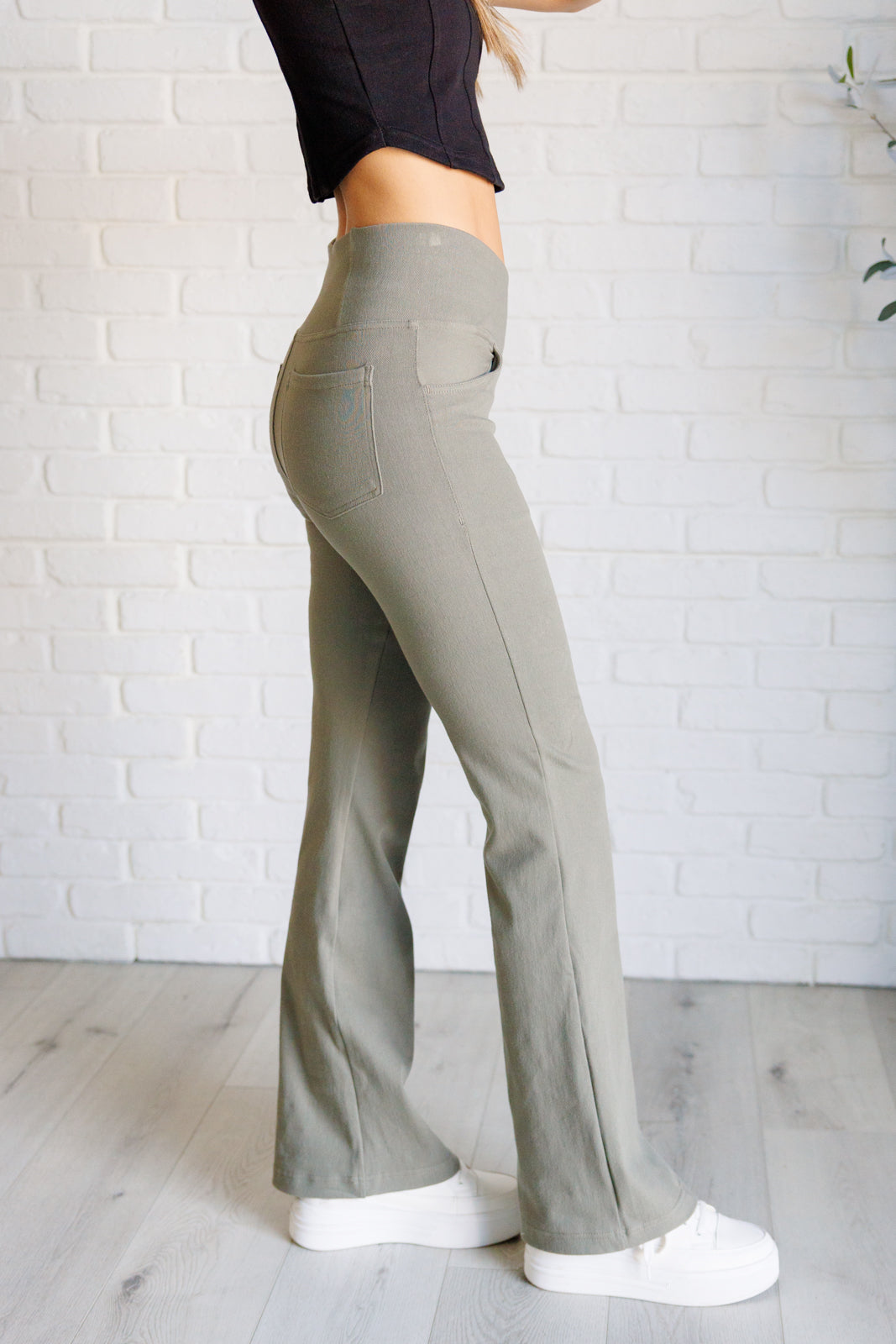 Side angle of person wearing dusty olive twill pants with flare and high waist standing on light wood floor