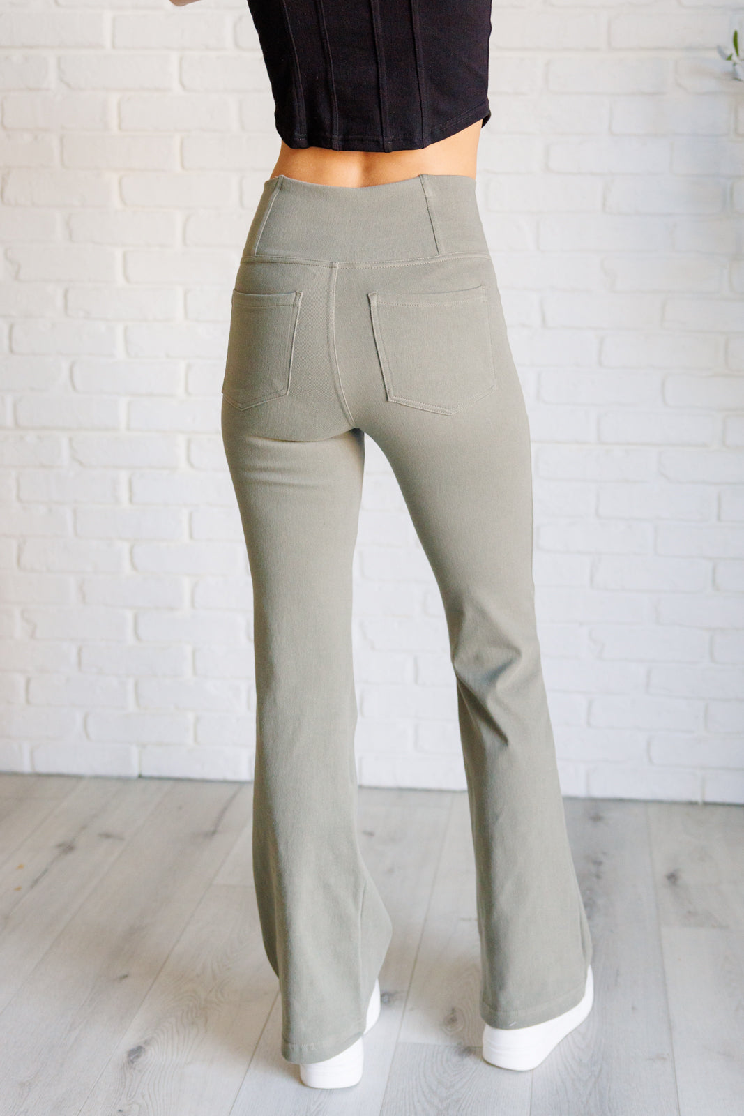 Back view of person wearing dusty olive high-waisted twill pants with flared legs standing on light wood floor