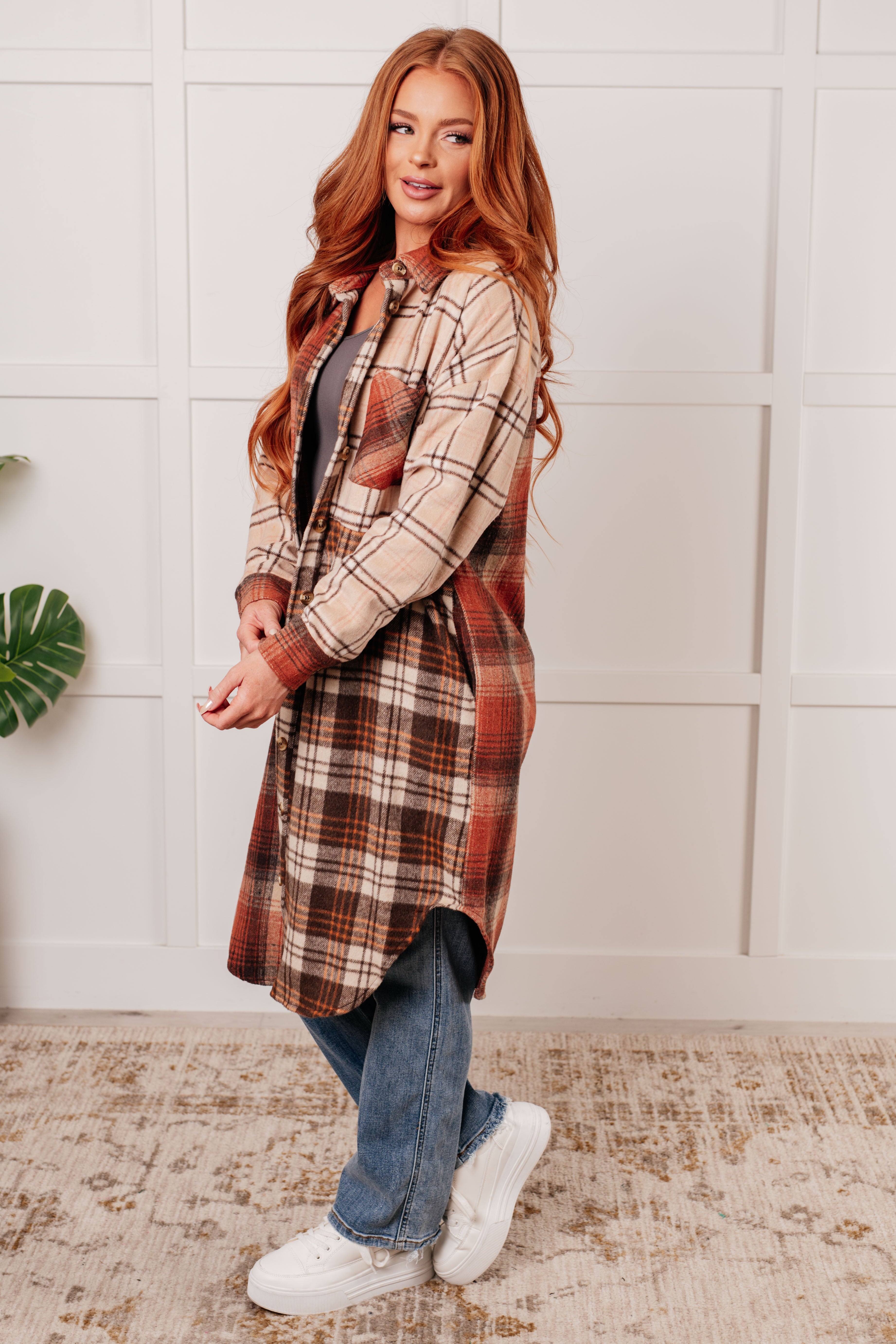 Side view of woman wearing long oversized plaid shacket in warm tones with rolled sleeves and blue jeans indoors
