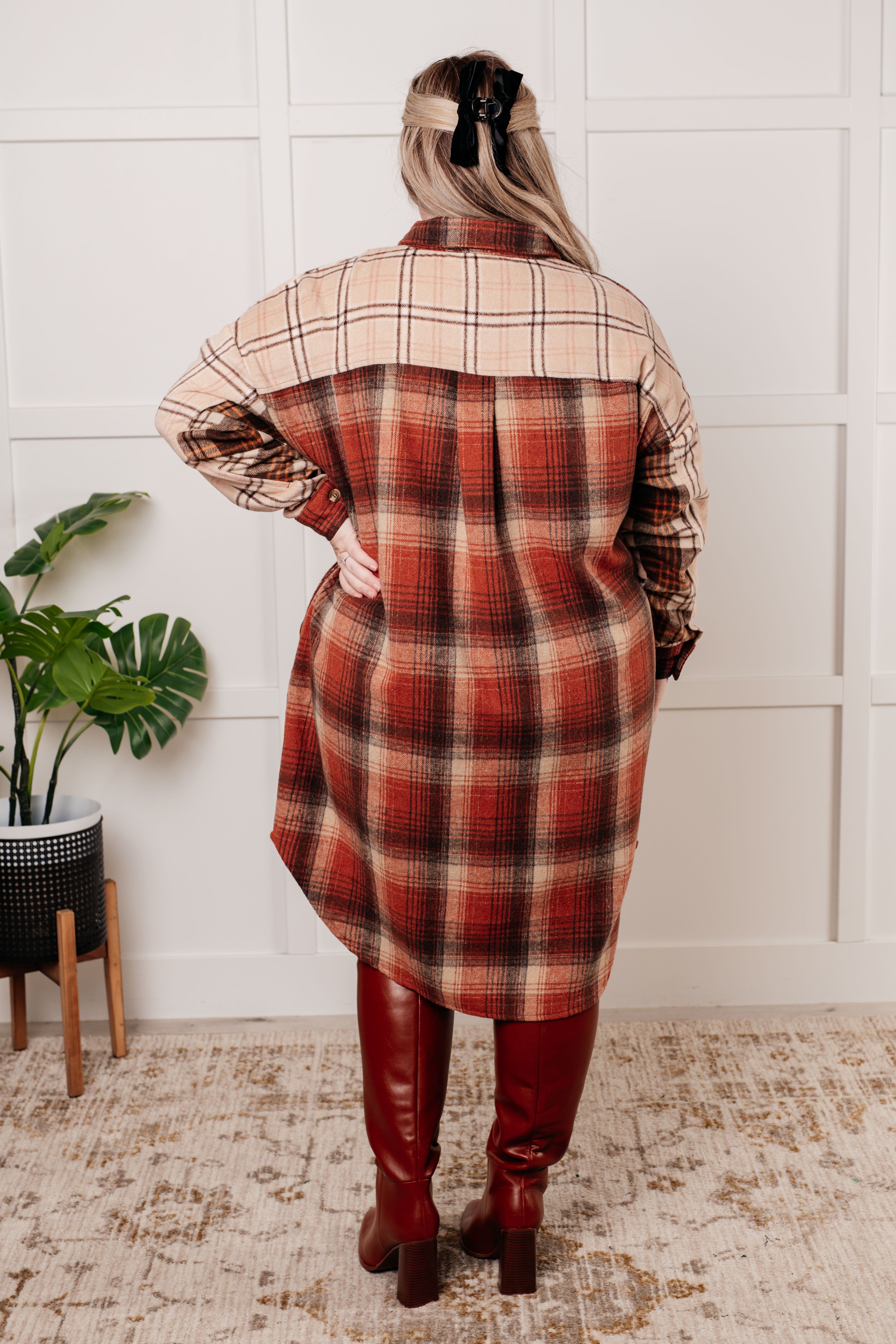 Back view of woman wearing oversized plaid flannel shacket with contrasting yoke and red knee-high boots indoors