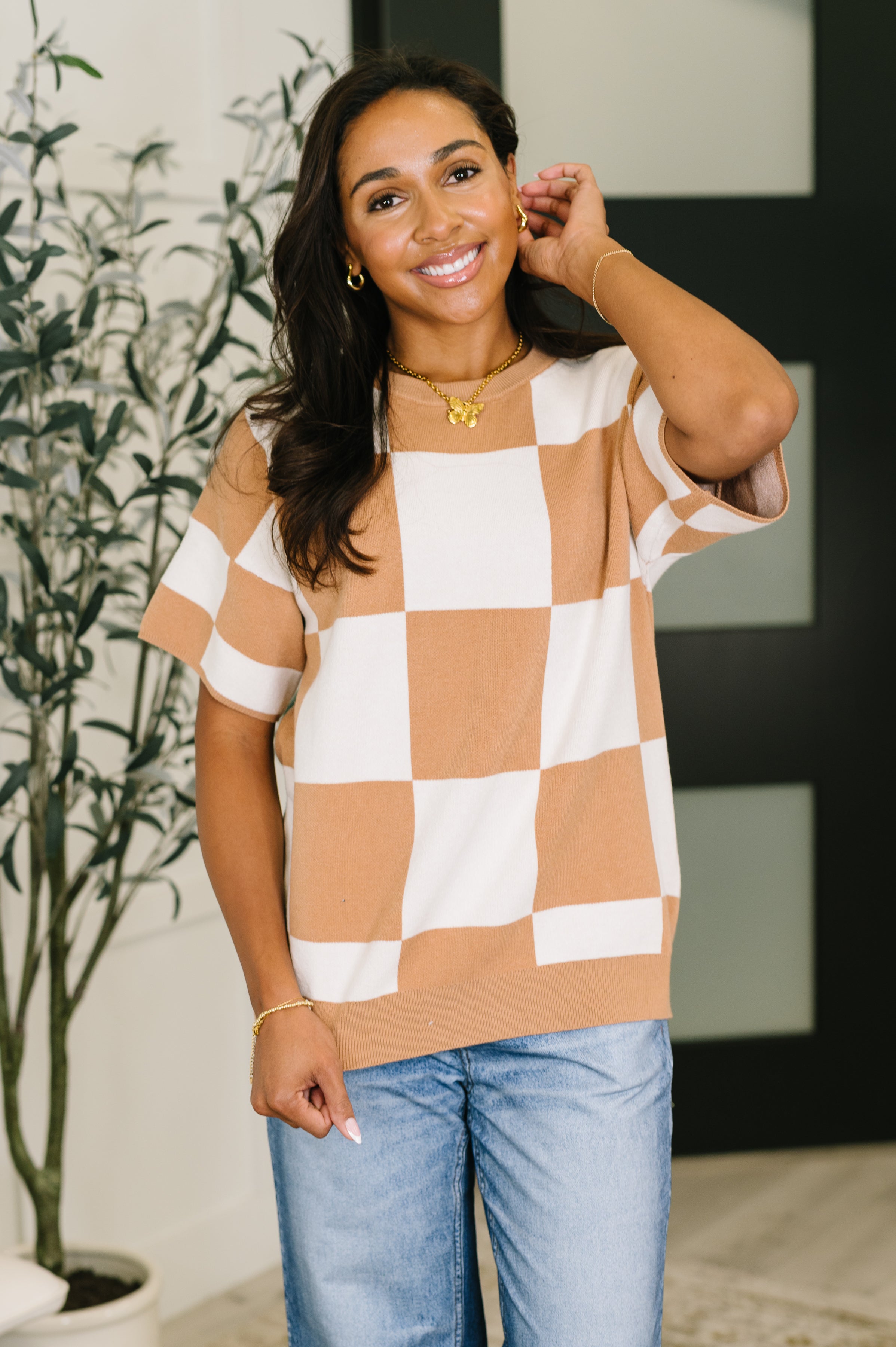 Smiling woman wearing cafe check short sleeve relaxed fit sweater paired with light wash jeans indoors