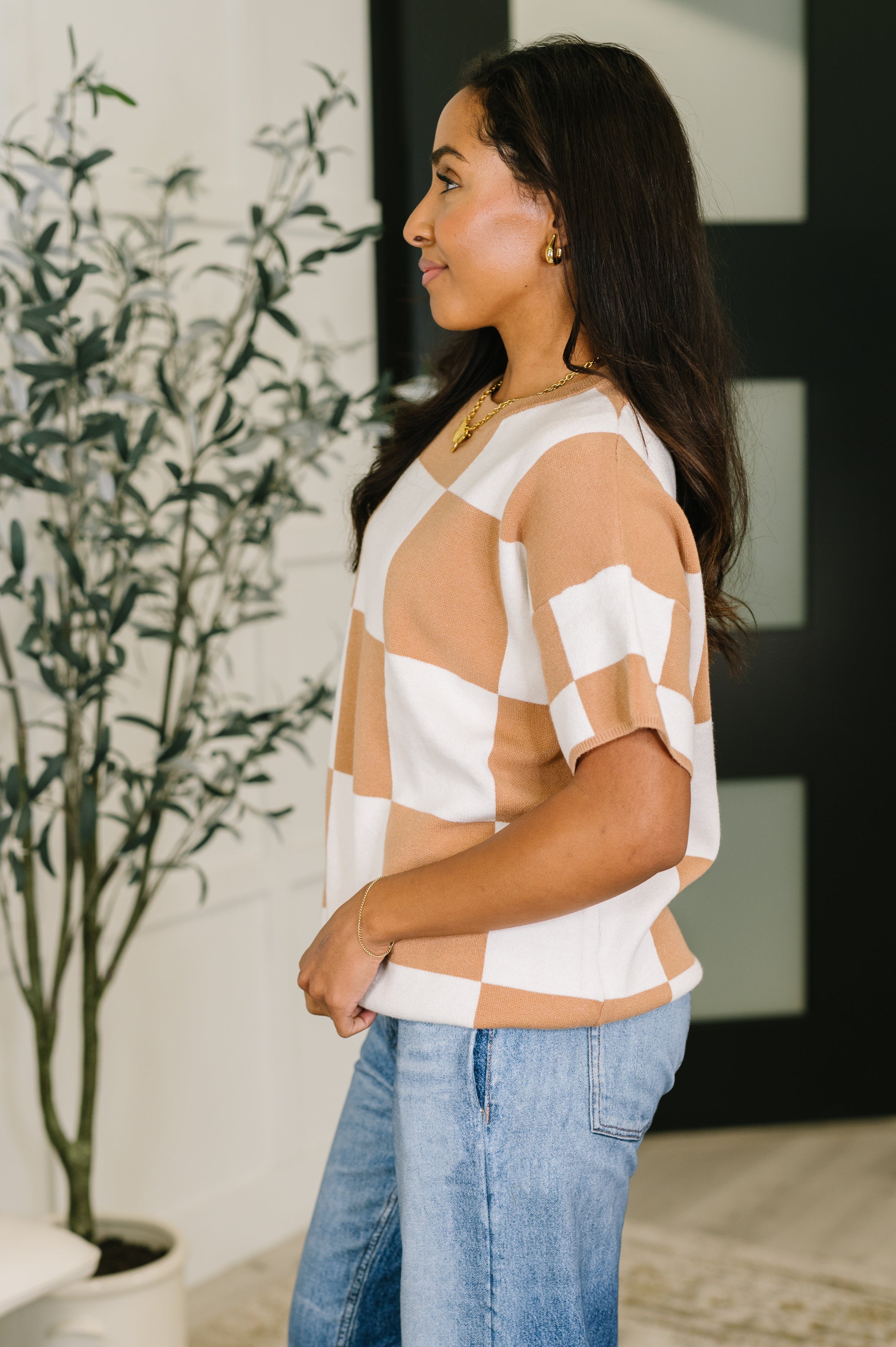 Woman modeling beige and white large checkered relaxed fit sweater with light blue jeans indoors