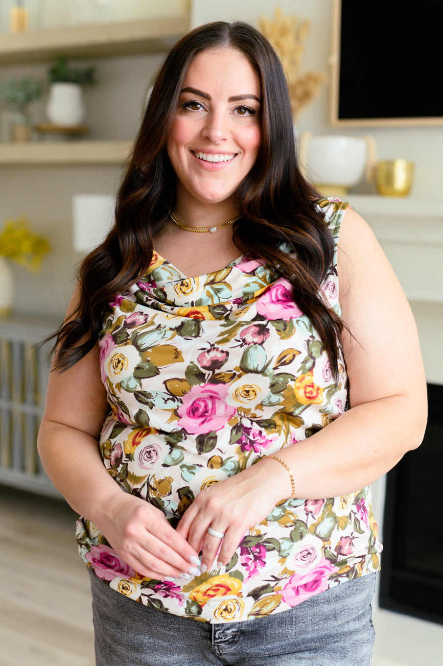 Smiling woman with long dark hair wearing floral cowl neck top in pink, yellow, and green tones indoors