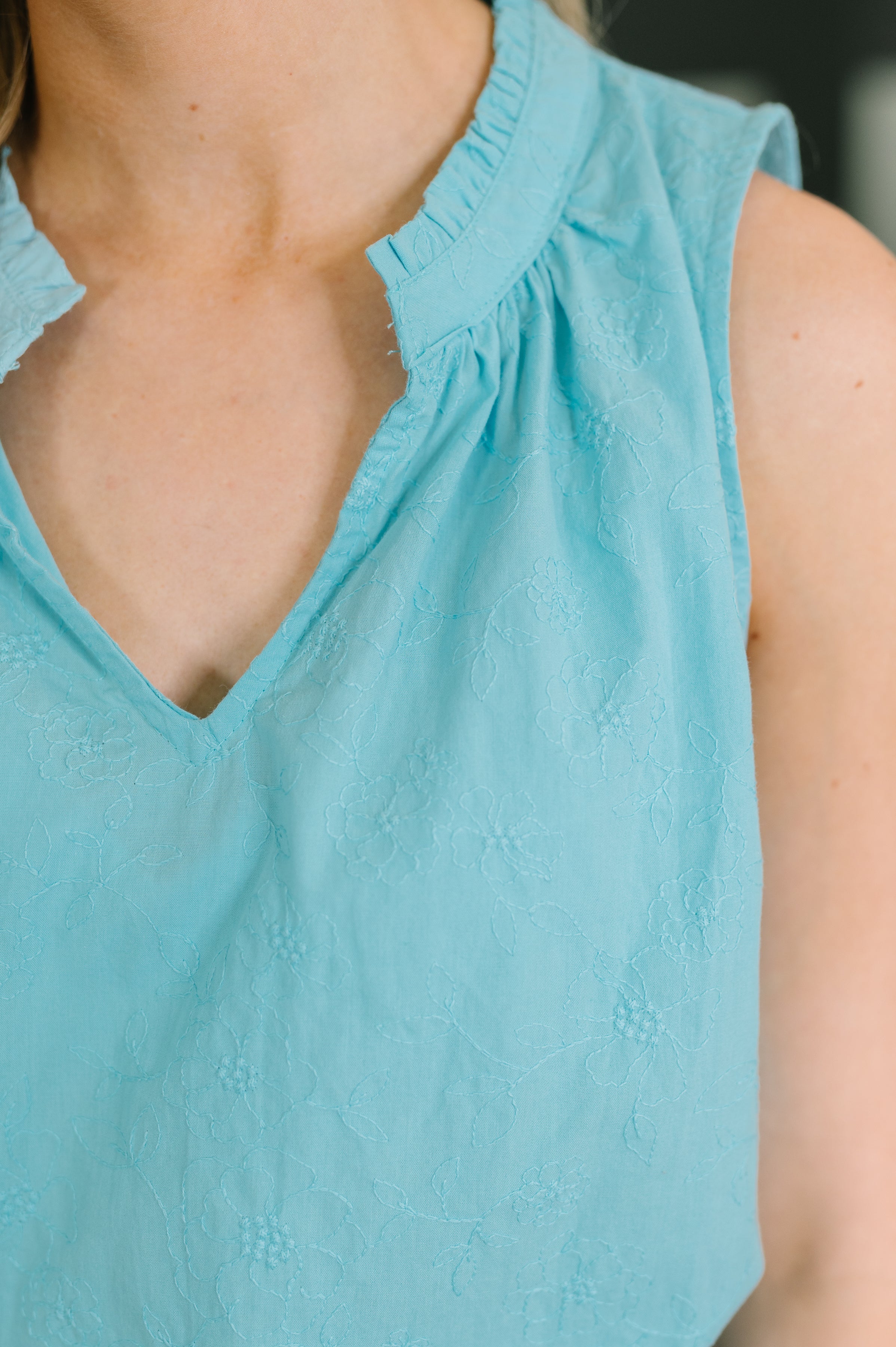 Close-up of sleeveless aqua top with split neckline and subtle floral embroidery on woven fabric