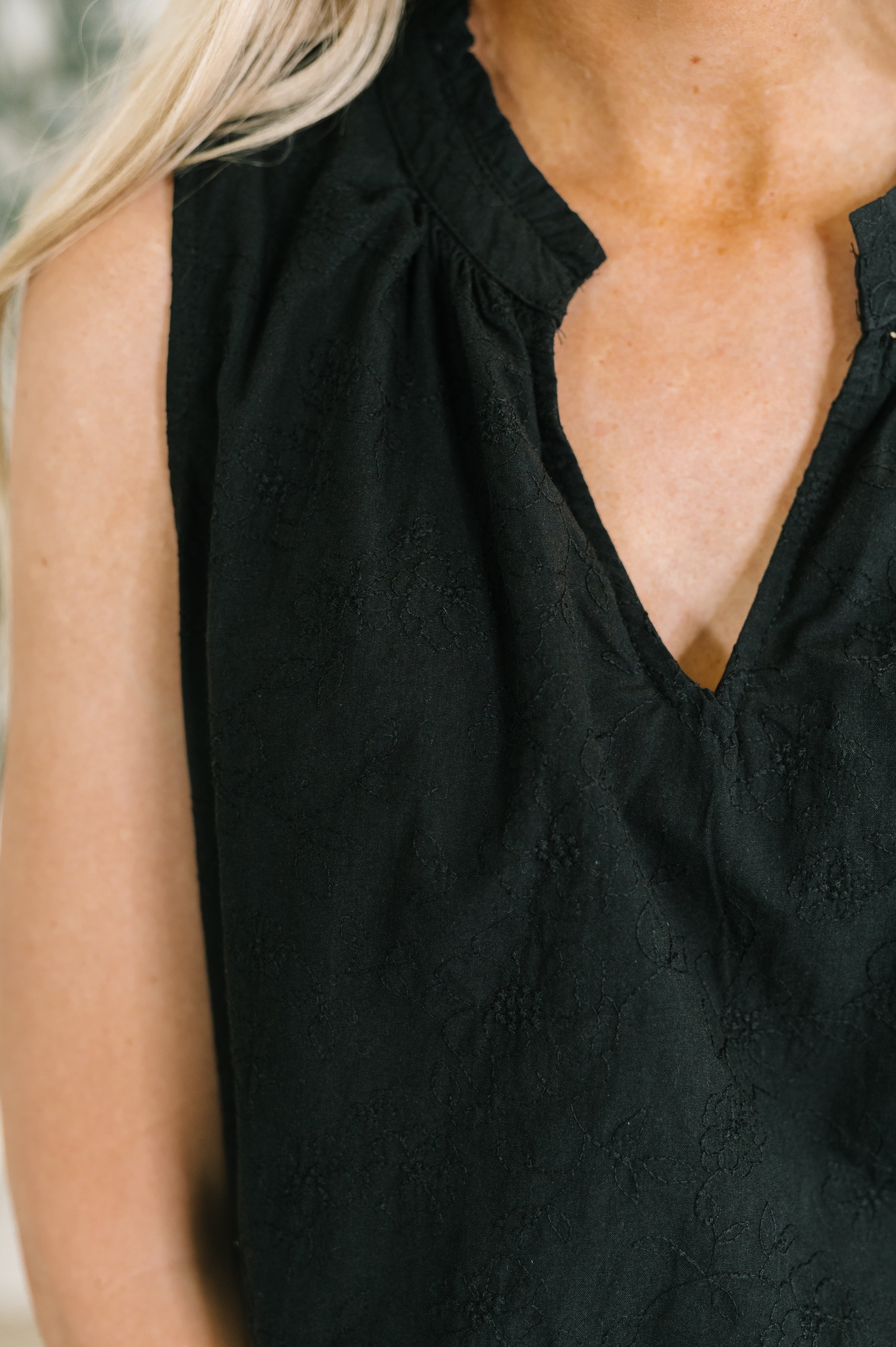 Close-up of sleeveless black tank with subtle floral embroidery and a soft split neckline on woven fabric