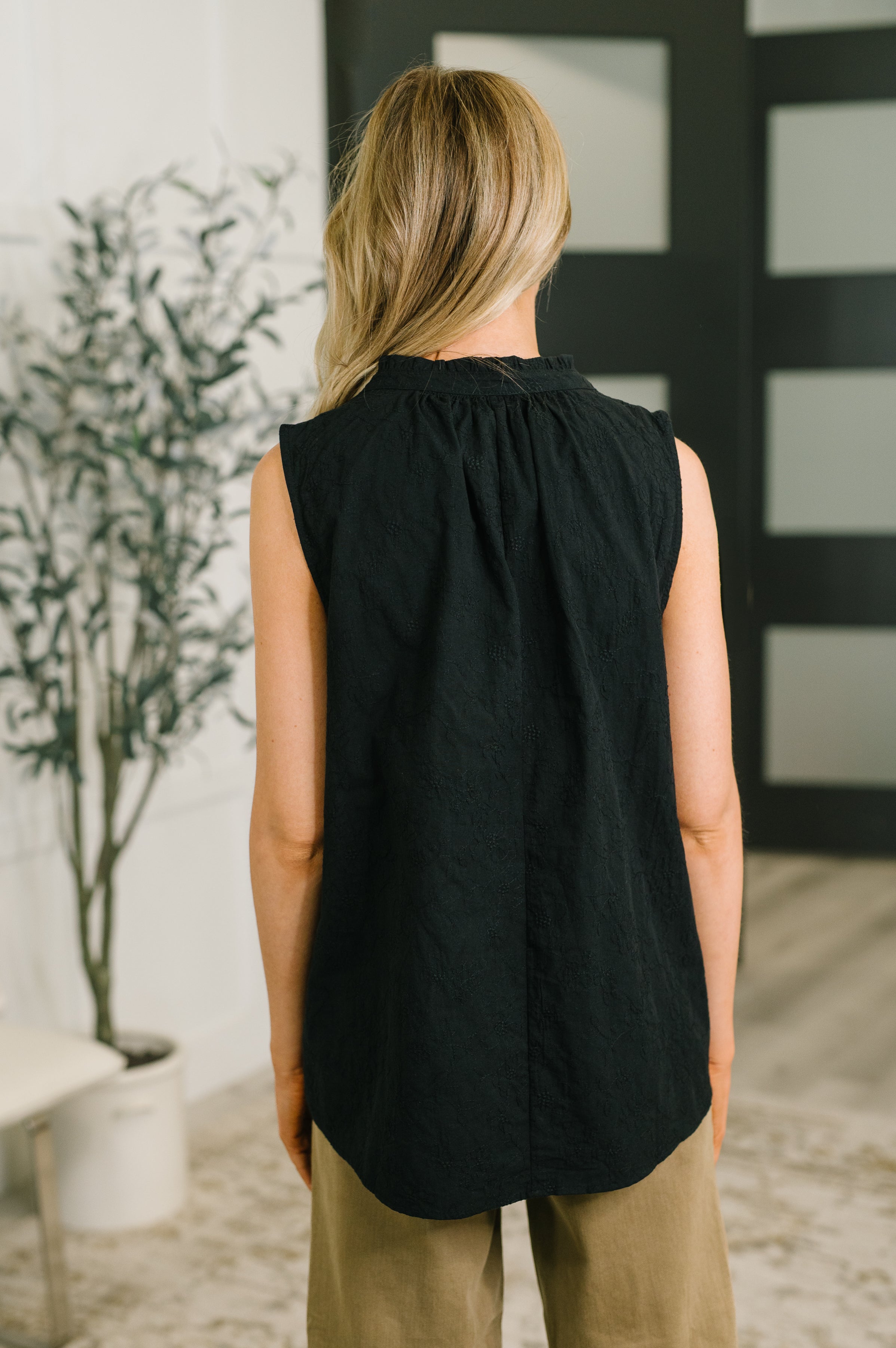 Back view of woman wearing sleeveless black embroidered tank with gathered neckline and relaxed fit indoors