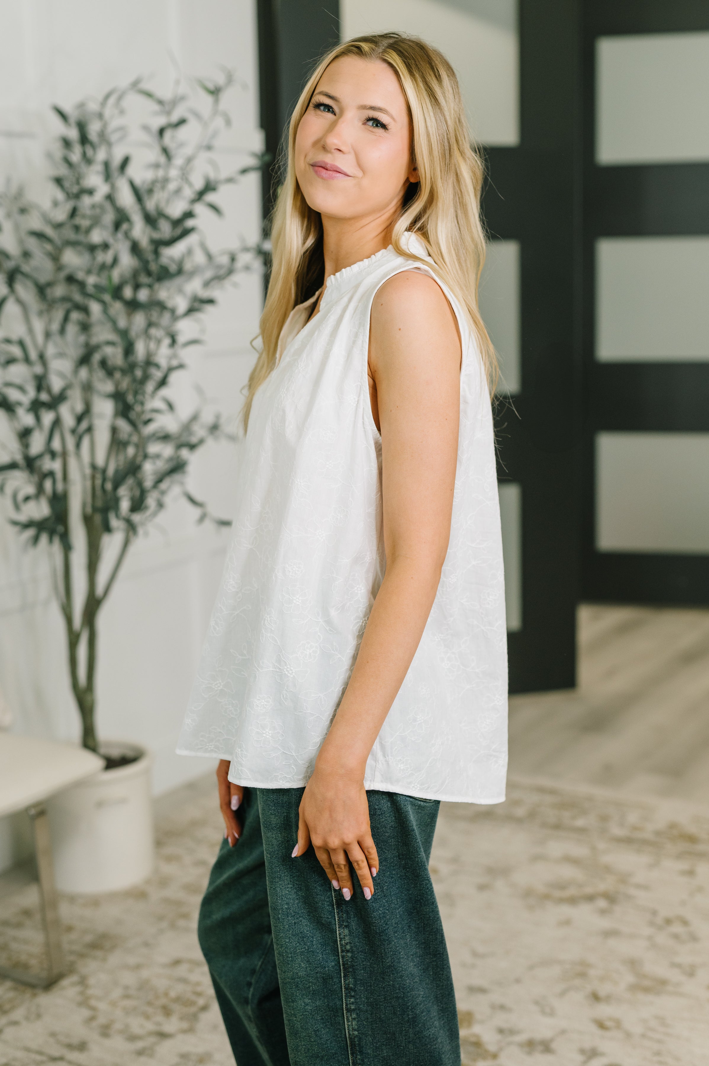 Side angle of woman wearing off white sleeveless embroidered tank with gathered neckline and relaxed fit indoors