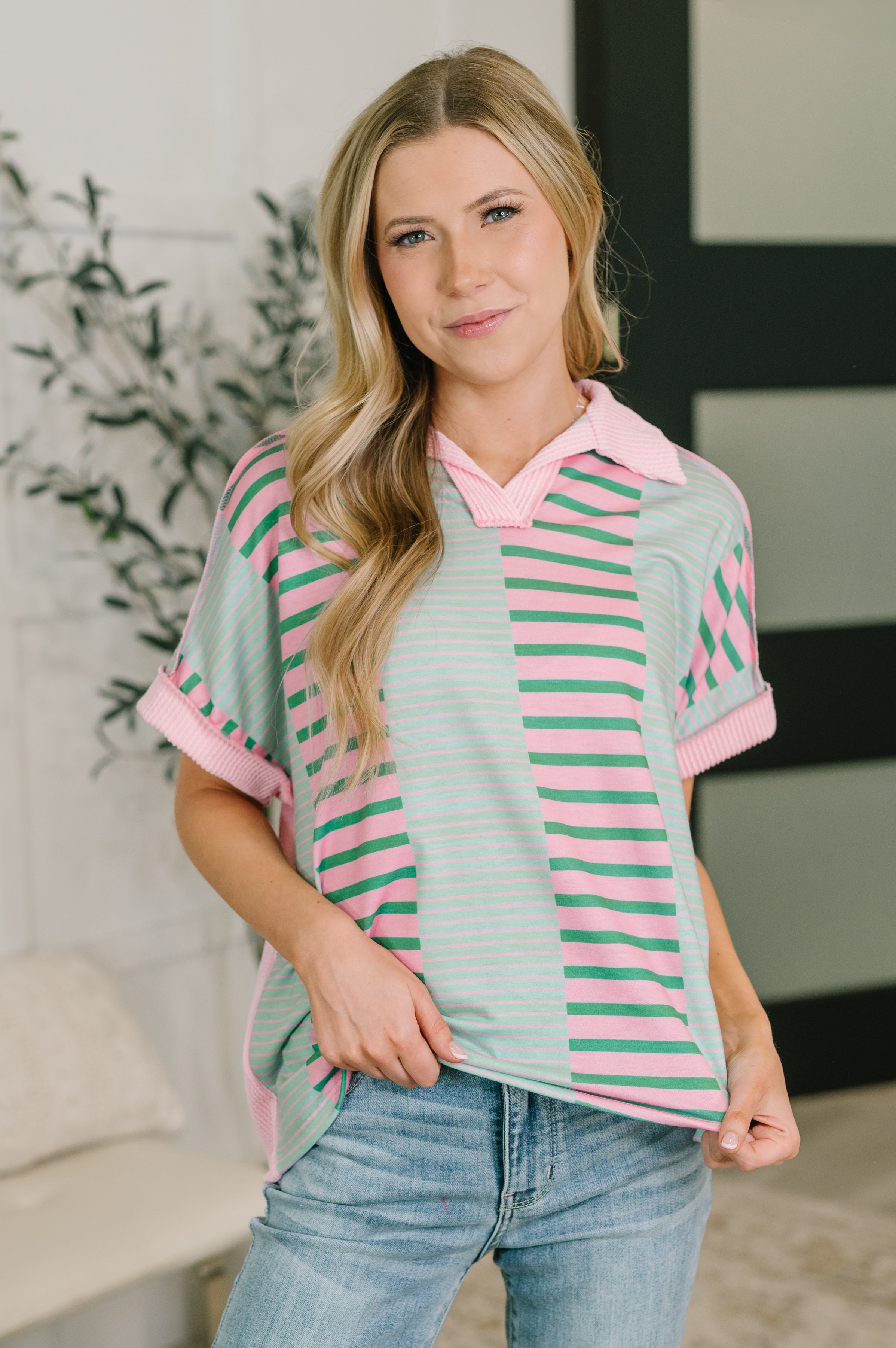 Woman wearing relaxed collared color block top with mint and pink stripes paired with light wash jeans indoors
