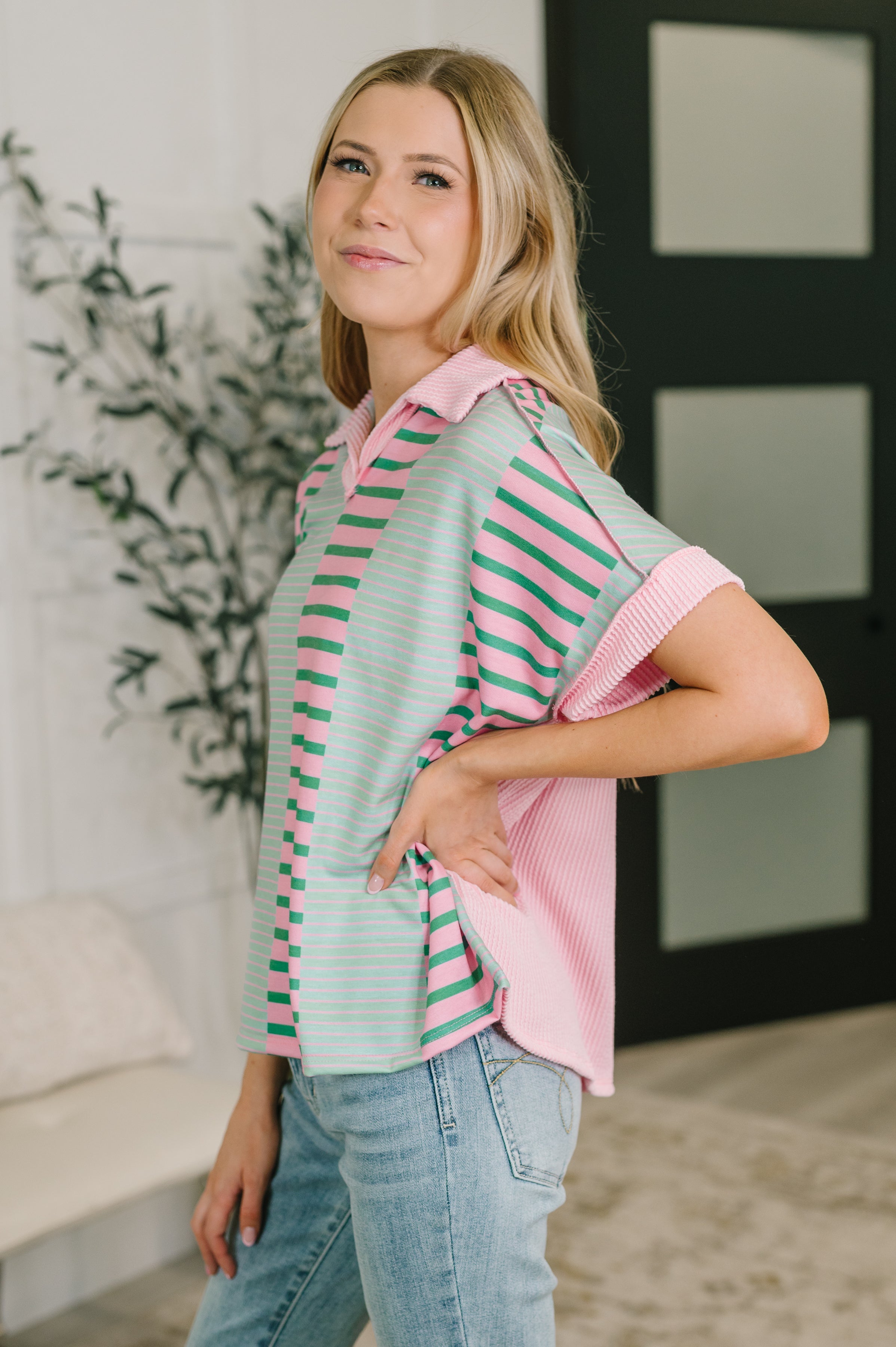 Side view of woman wearing pastel pink and mint striped collared top with short sleeves in casual indoor setting
