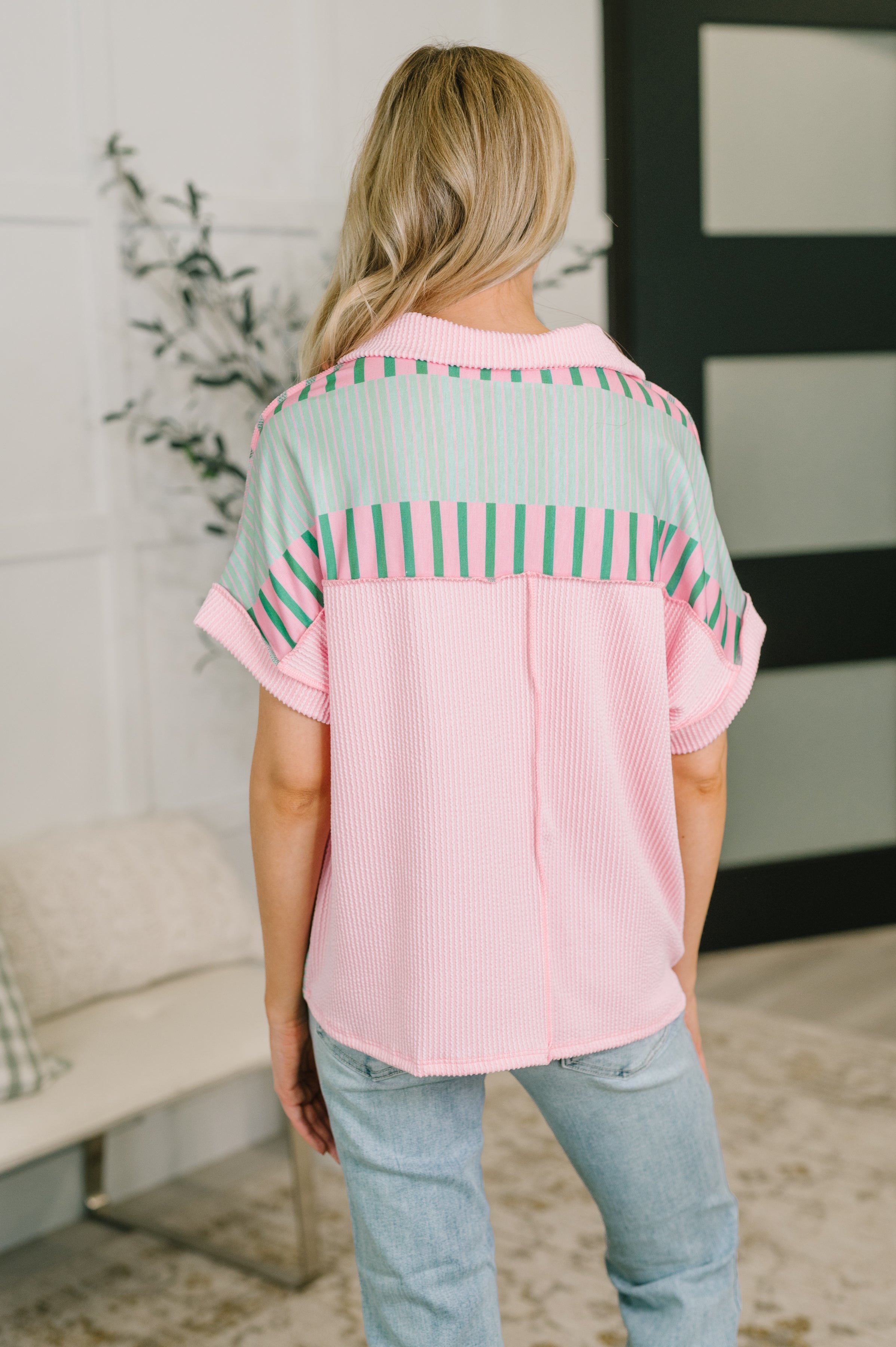 Back view of woman wearing pink collared top with mint and green color block stripes in cozy indoor setting