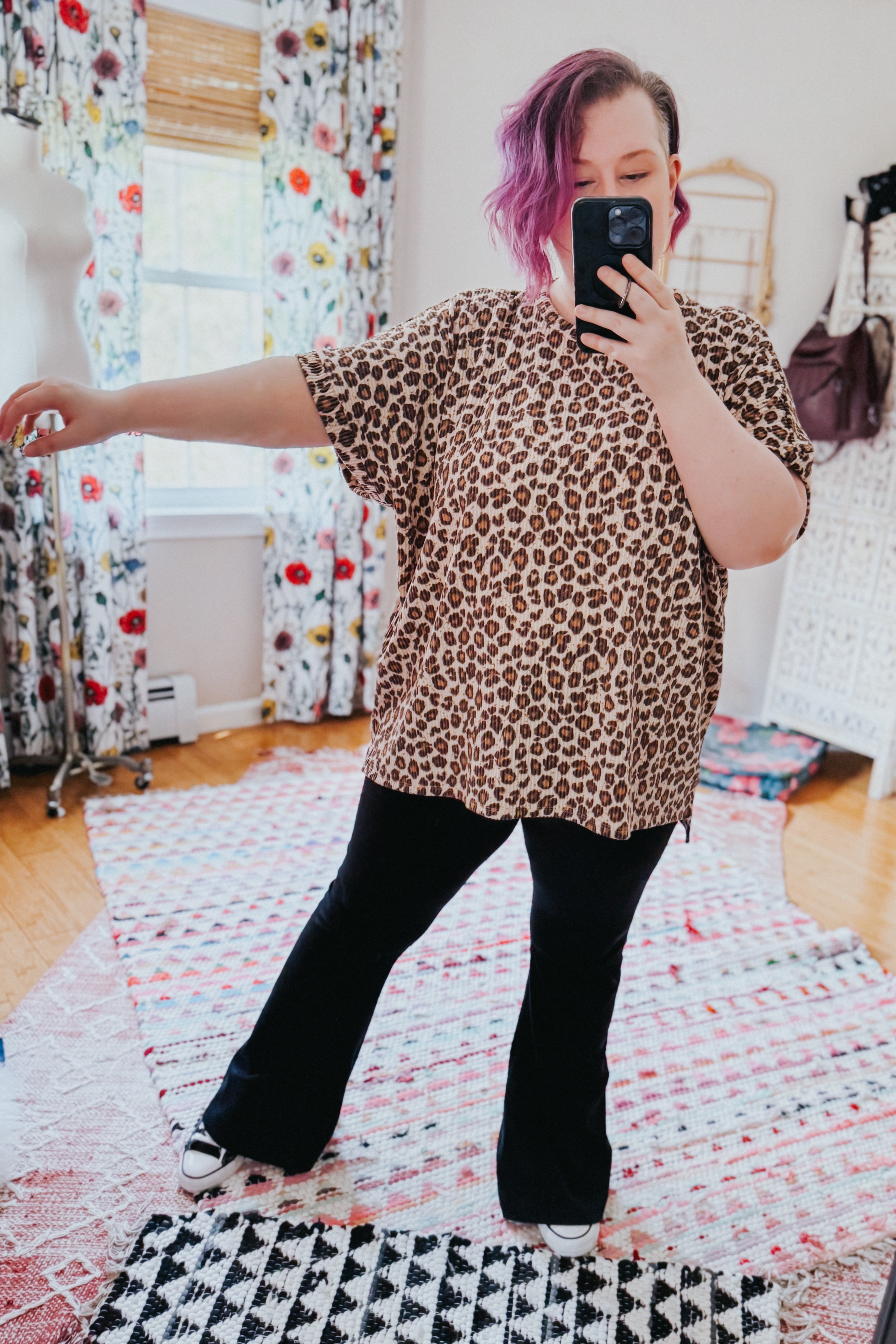 Woman wearing loose leopard print short-sleeve top paired with black flared pants and white sneakers inside a bright room