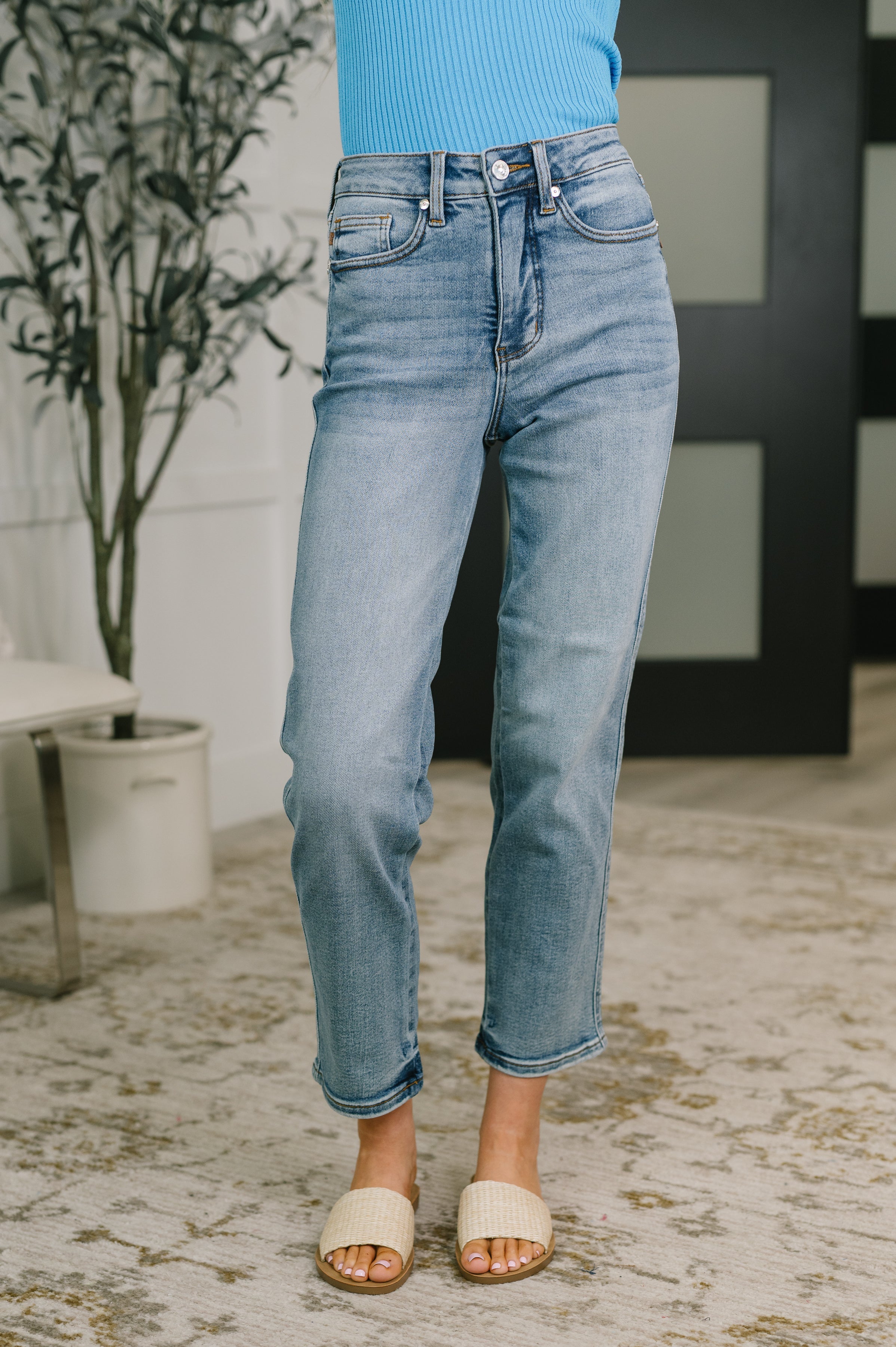 Front view of person wearing medium wash blue high waist straight jeans with rolled hems and beige slide sandals indoors