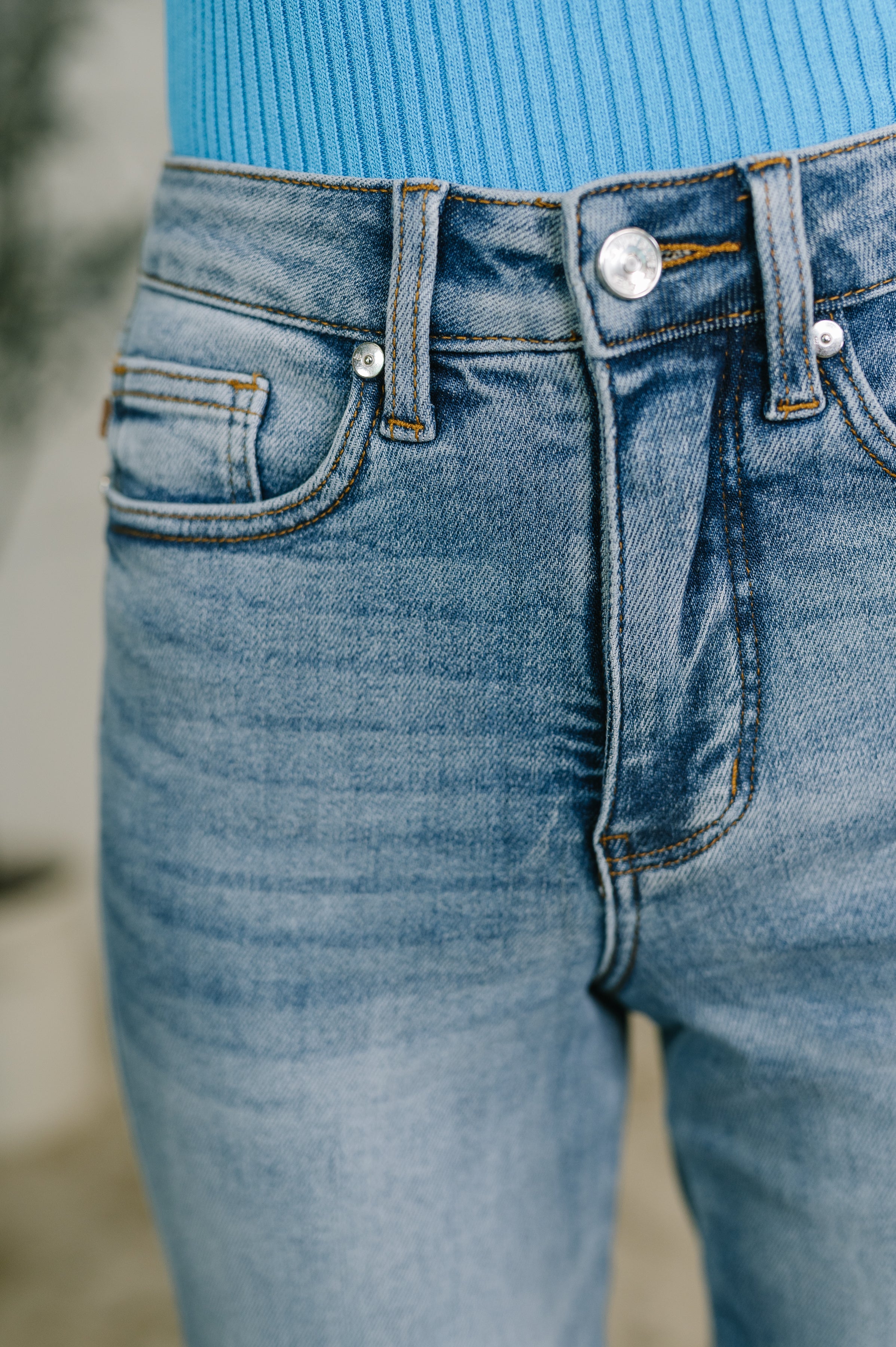 Close-up of medium wash blue denim jeans with front pockets and button closure paired with blue ribbed top