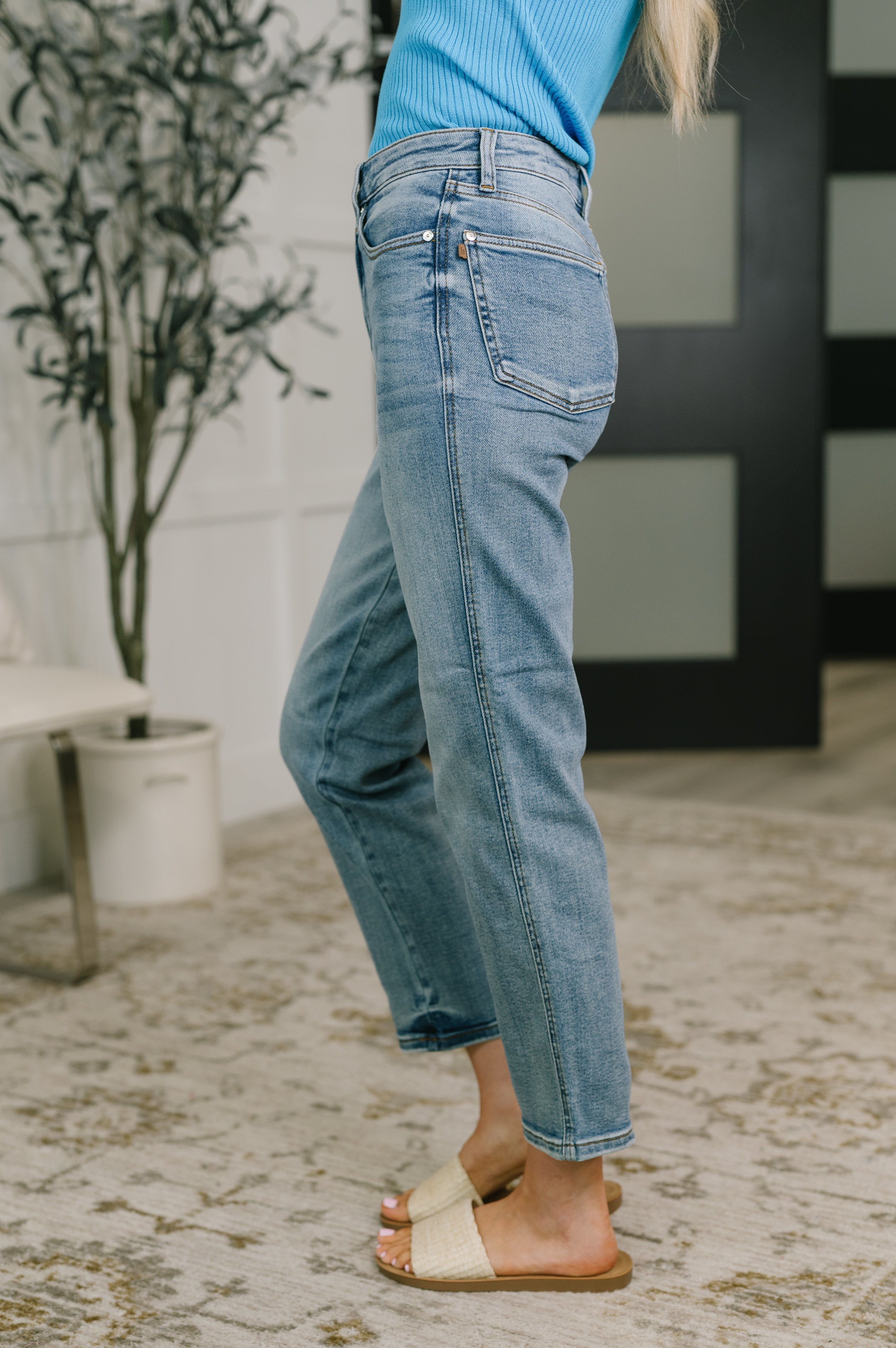 Side view of woman wearing medium wash blue high waist ankle straight jeans with woven slide sandals indoors