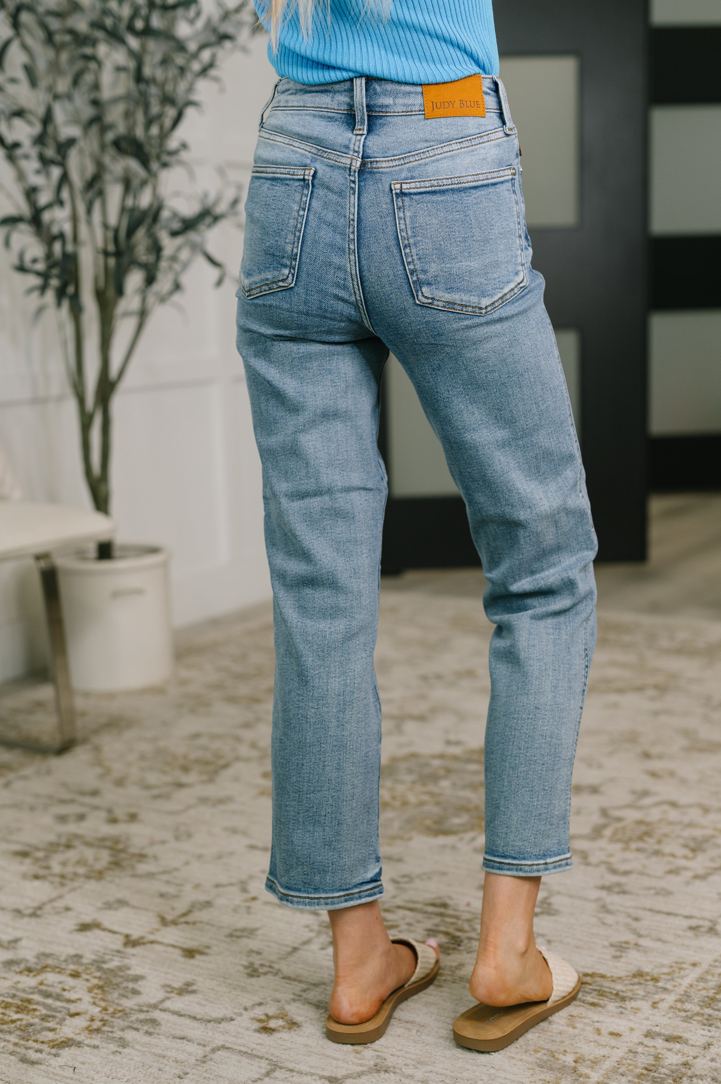 Rear view of woman wearing medium wash blue high-waist straight jeans with ankle length indoors standing on rug
