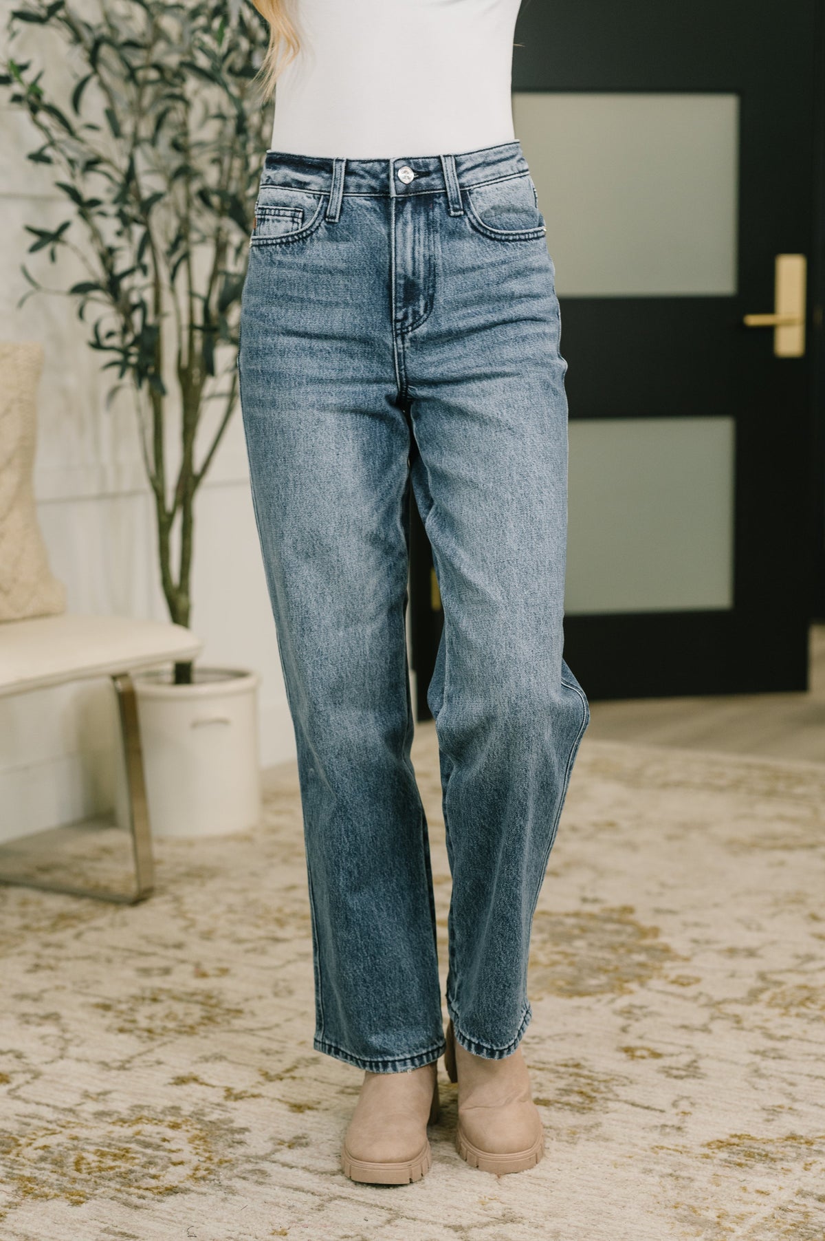 High waist blue straight leg jeans styled with a white top and neutral flats in a softly decorated indoor setting