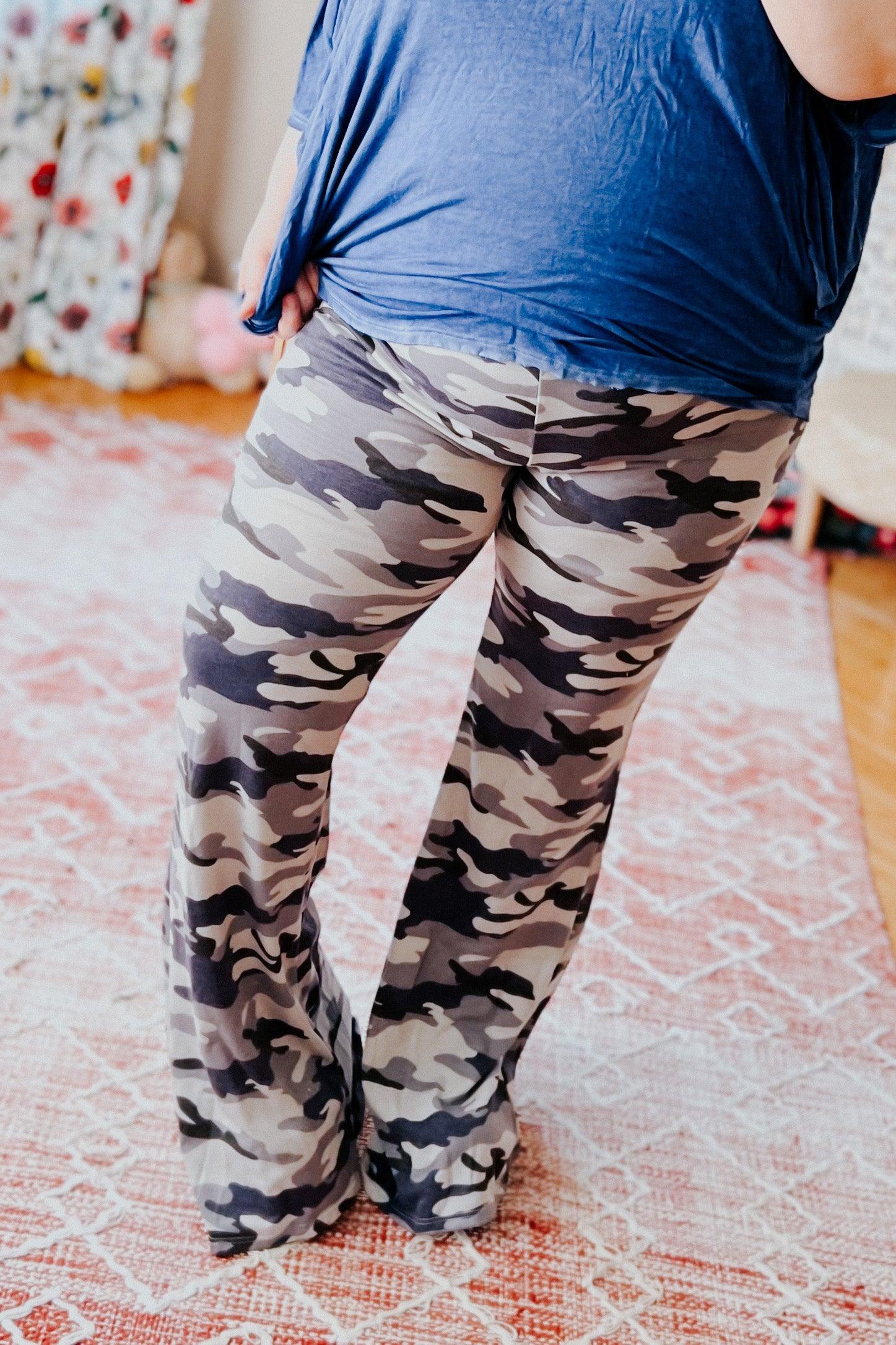 Woman wearing relaxed fit flare pants with grey and navy blue camouflage print standing on patterned rug indoors