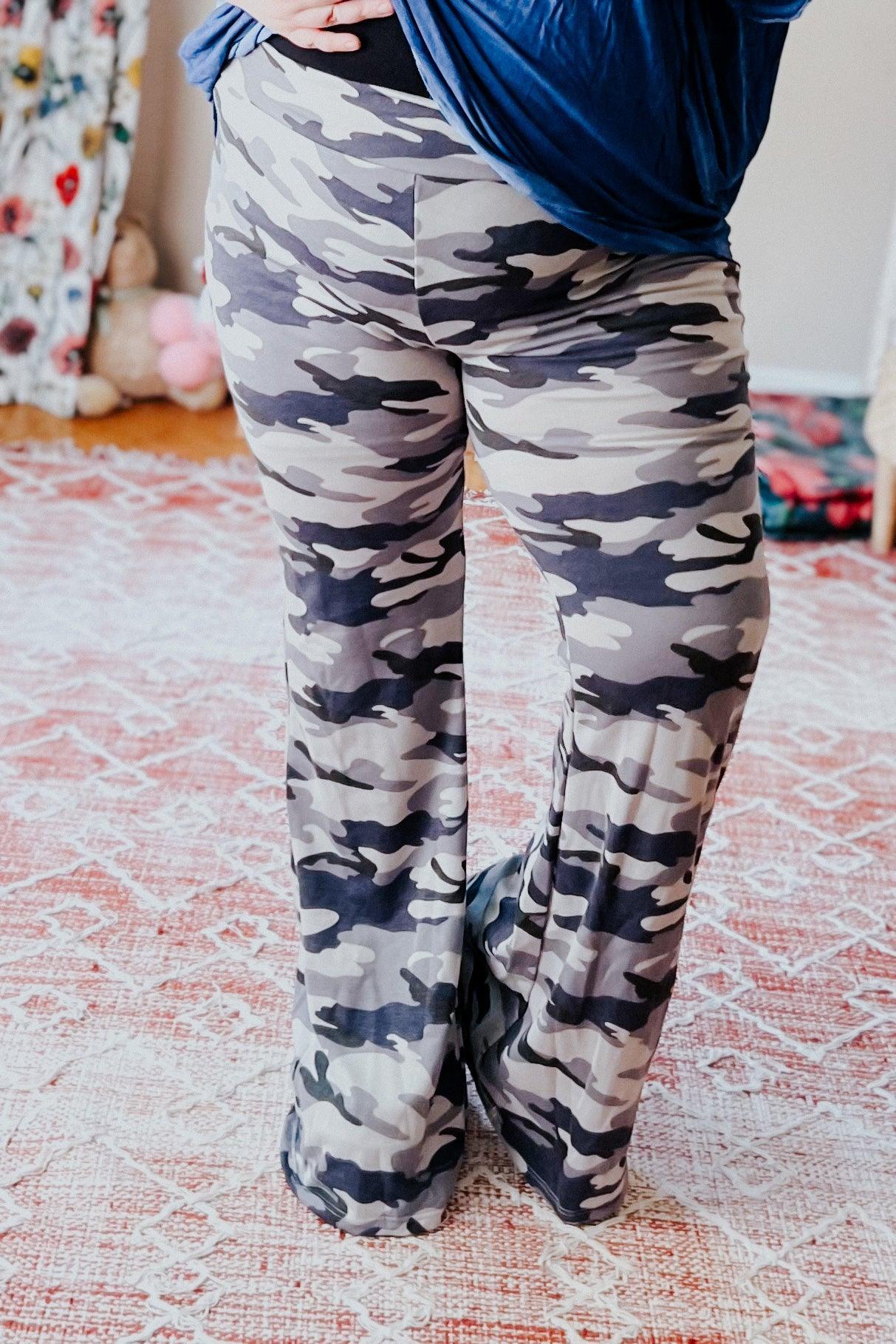 Close-up of woman wearing grey and navy blue camouflage flare pants standing on patterned rug indoors