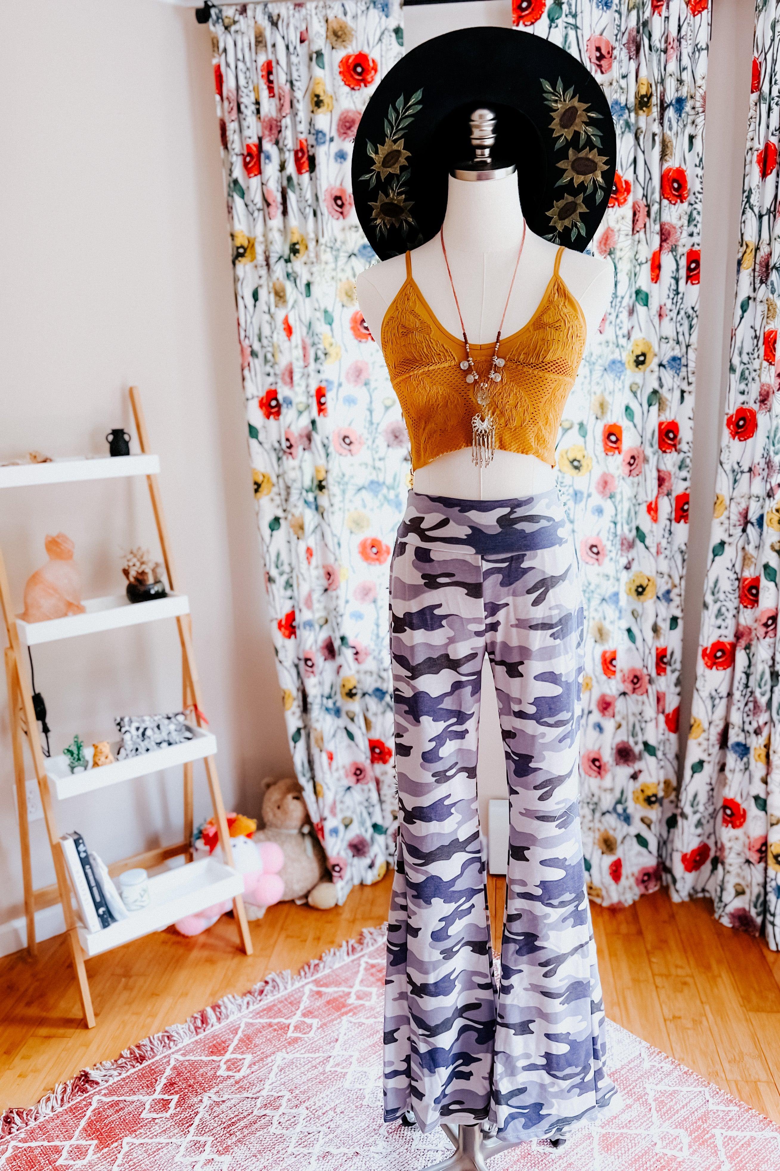 Mannequin dressed in grey and navy blue camo flare pants and mustard crop top against floral curtains in bright room