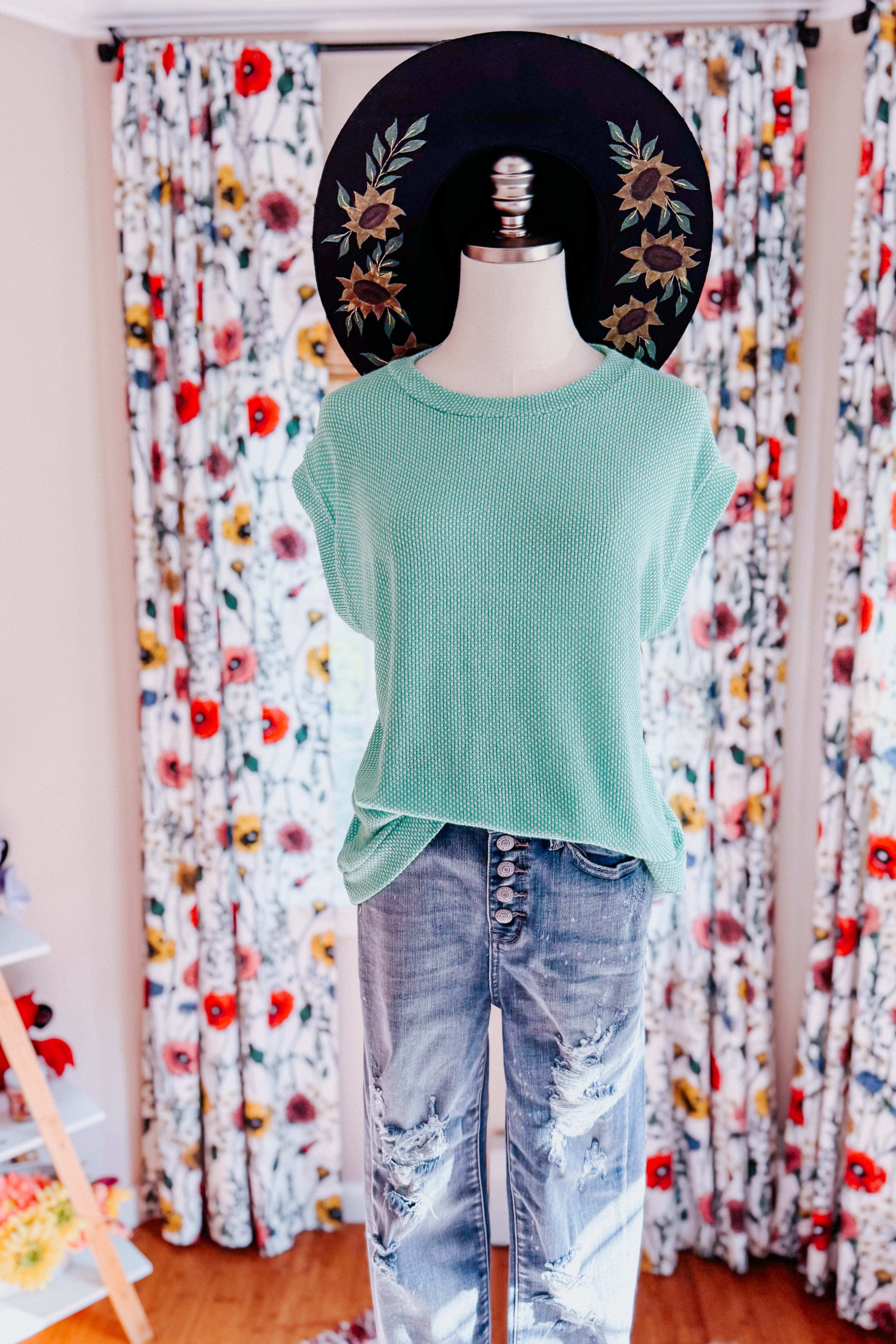 Mannequin wearing mint waffle knit sleeveless top paired with distressed high-waisted jeans and black hat with floral embroidery