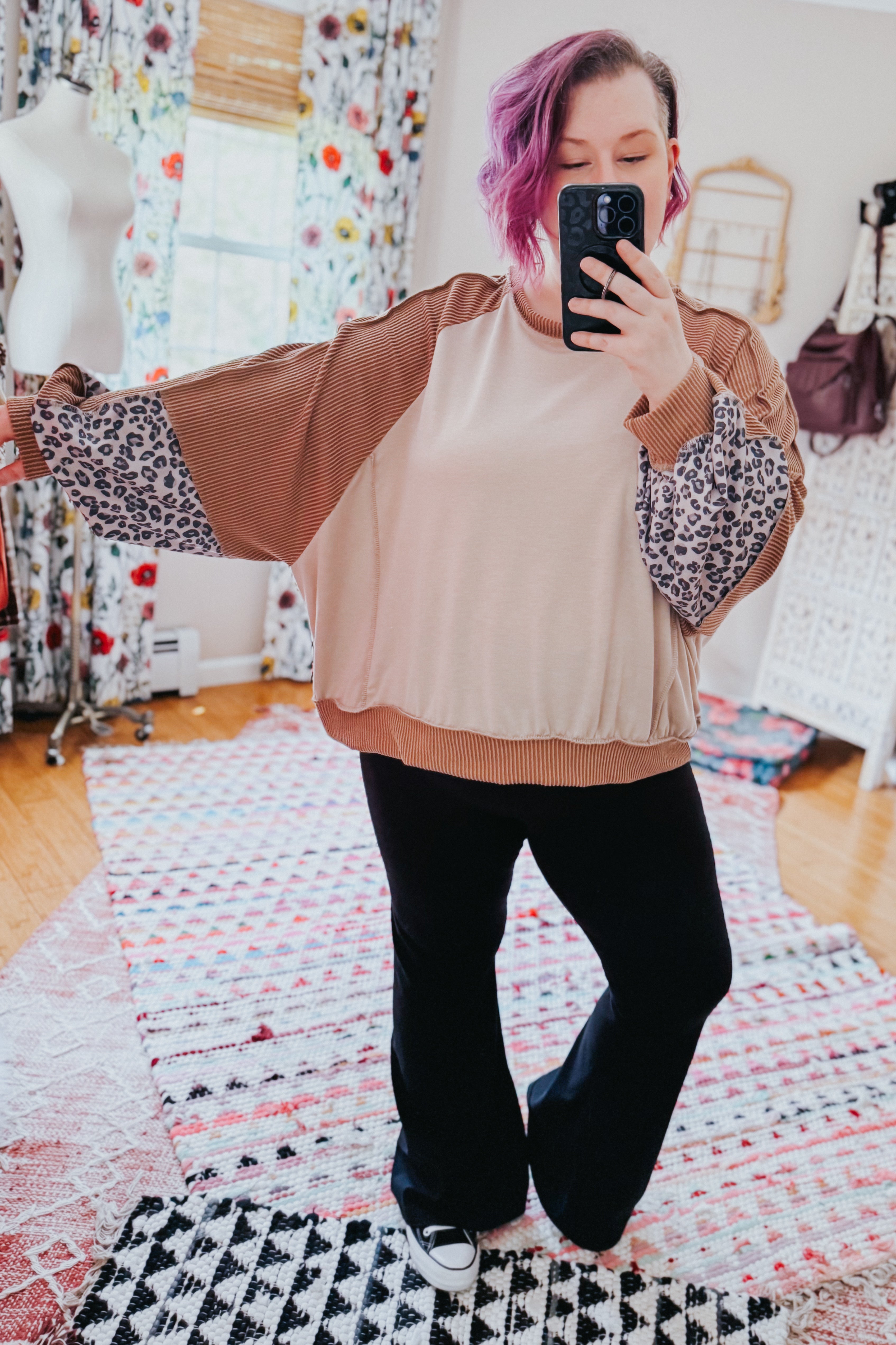 Woman taking mirror selfie wearing beige dolman colorblock top with brown ribbed and leopard print sleeves paired with black pants