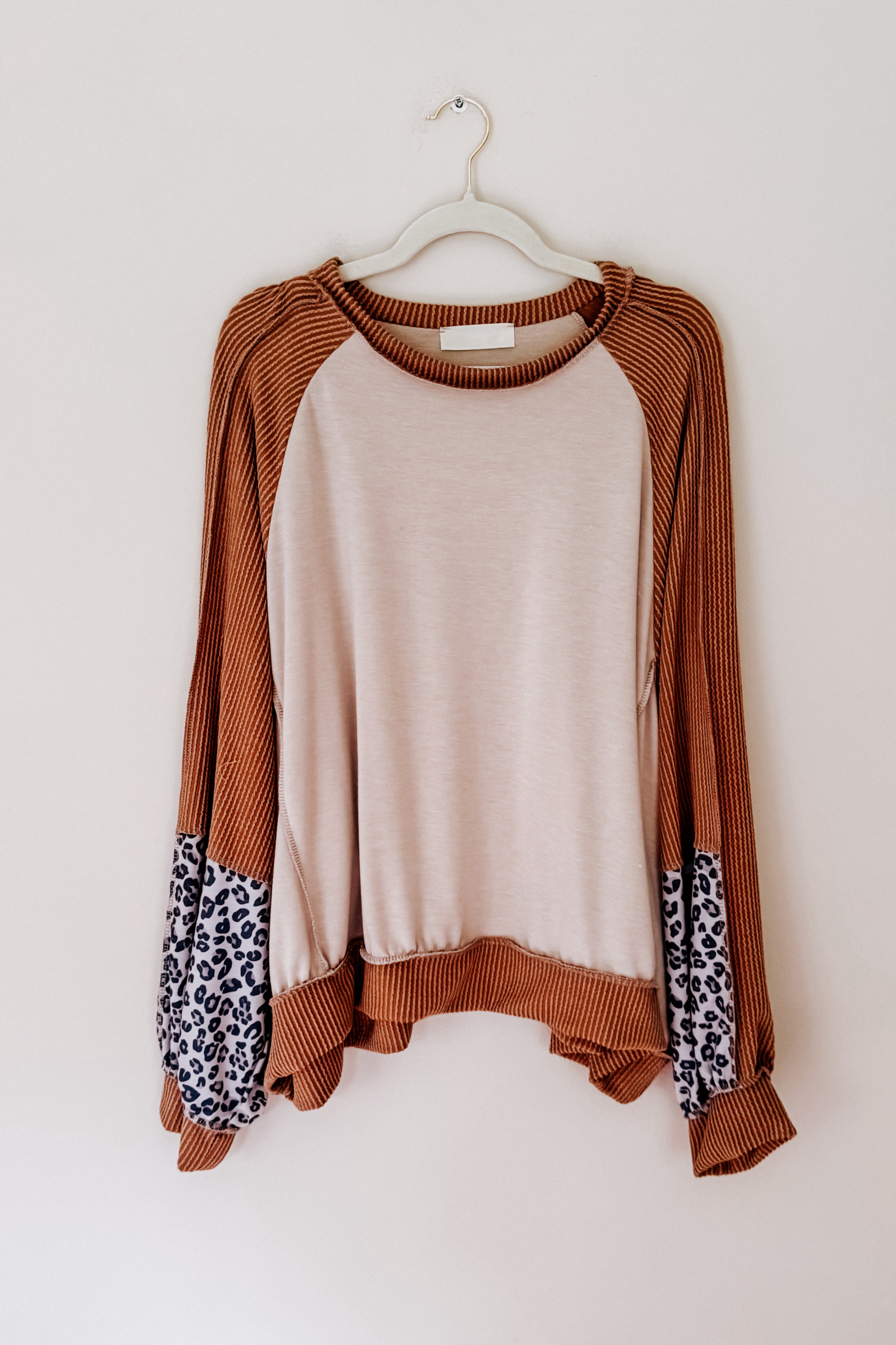 Dolman sleeve colorblock top with beige center, rust ribbed sleeves, and leopard print panels hanging on white hanger