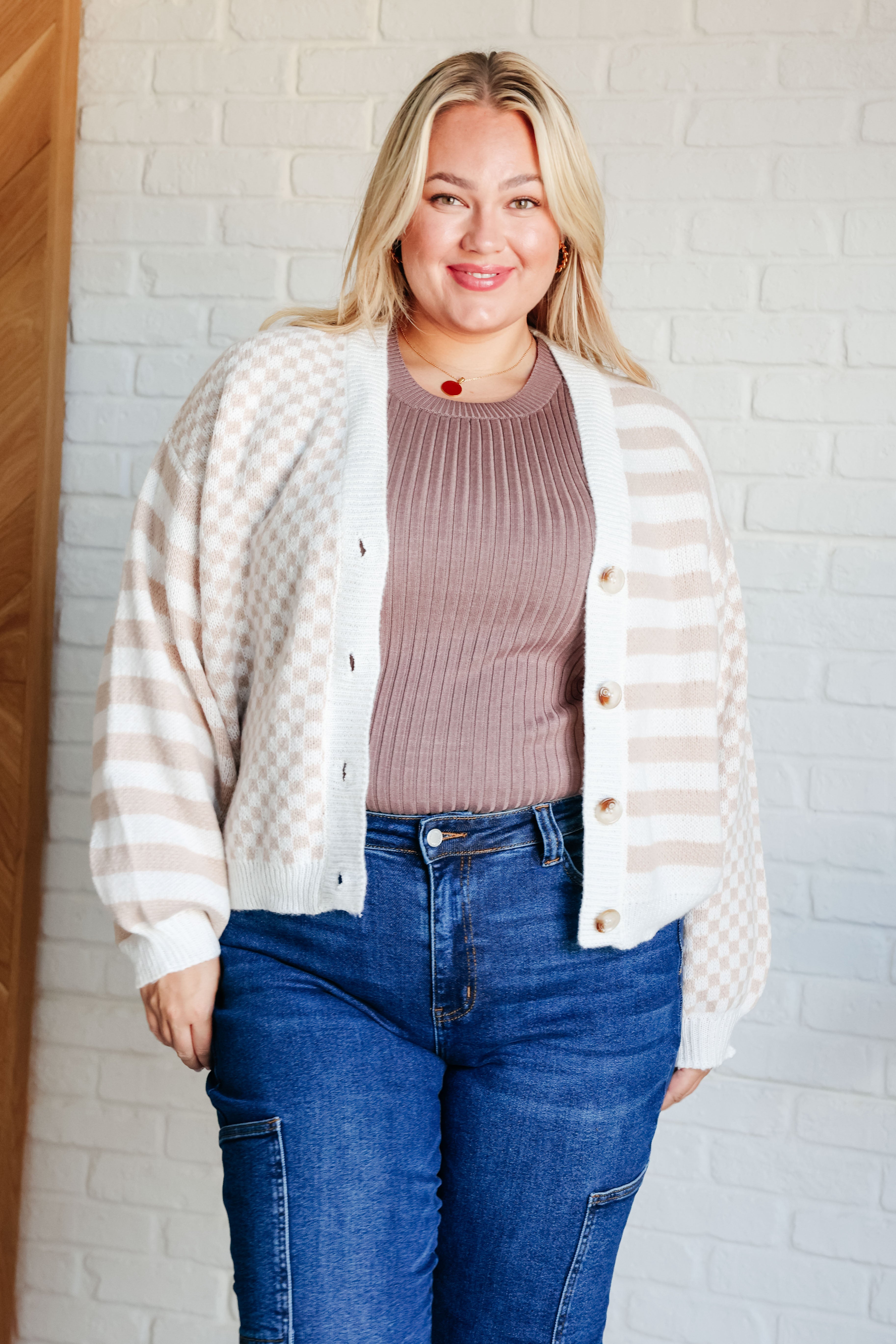 Smiling woman wearing beige and white cardigan with mixed checkered and striped patterns paired with blue jeans
