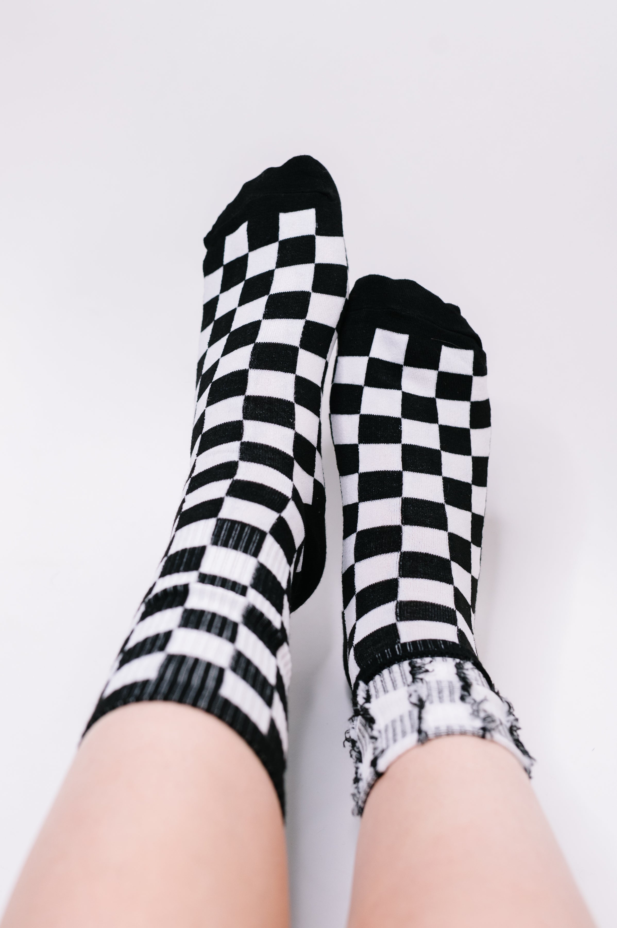 Pair of feet wearing mismatched black and white checkered quarter socks against plain background