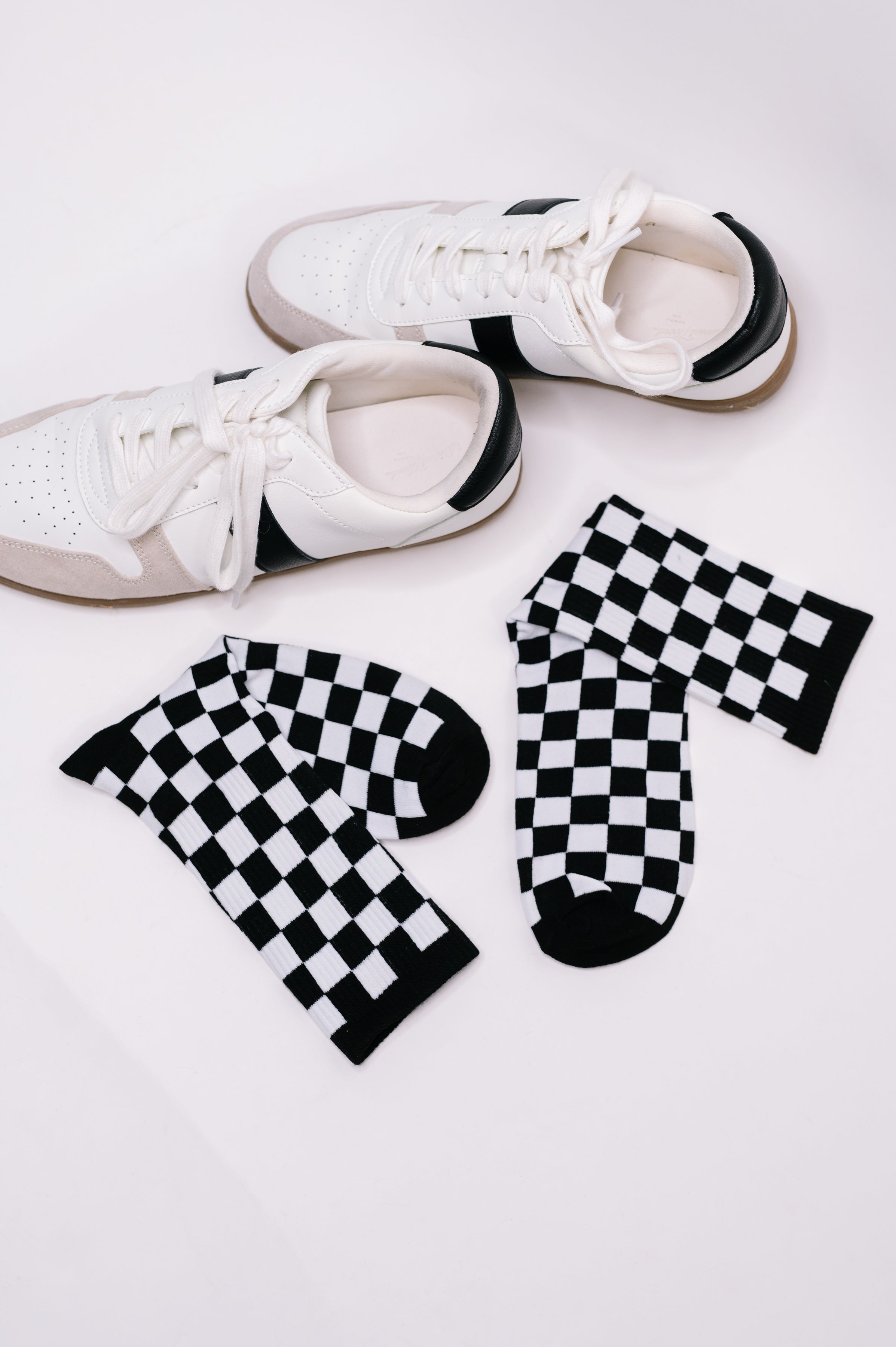Pair of black and white checkered quarter socks placed next to white sneakers with black accents on white background