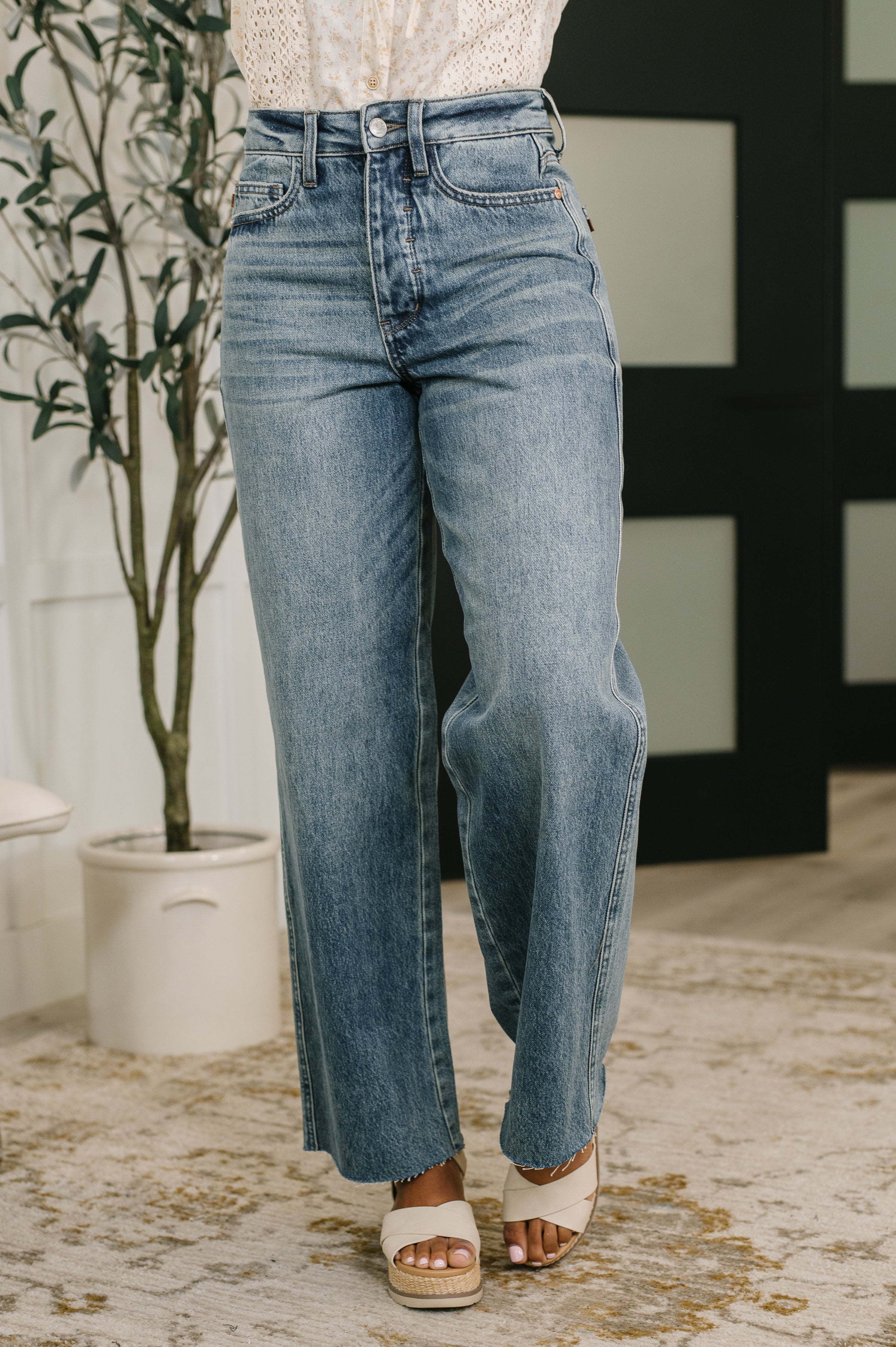 Blue high waist baggy jeans styled with a white top and beige platform sandals in a light, cozy room setting