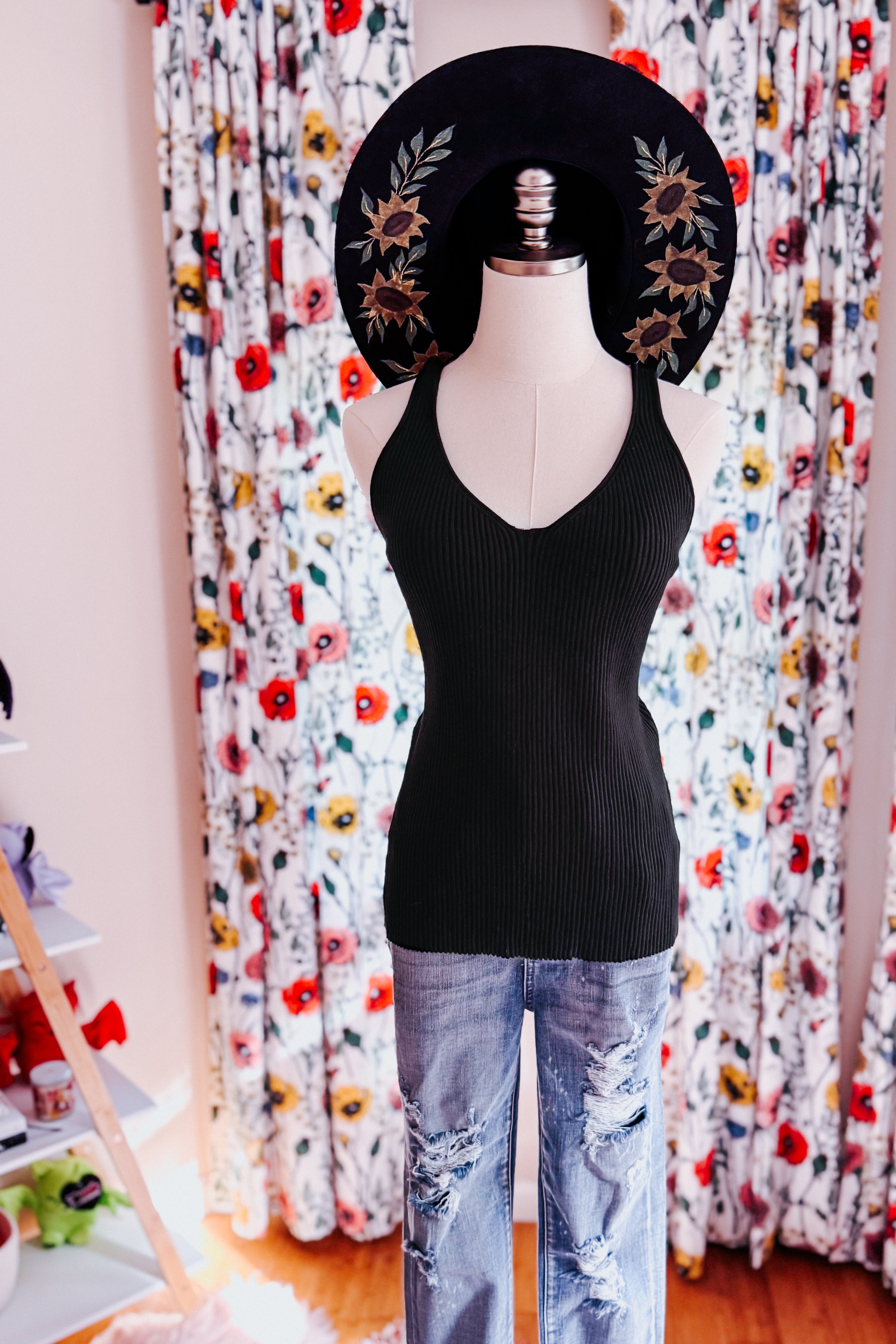 Black ribbed tank top styled with distressed light wash jeans and a wide-brimmed hat with floral embroidery on mannequin
