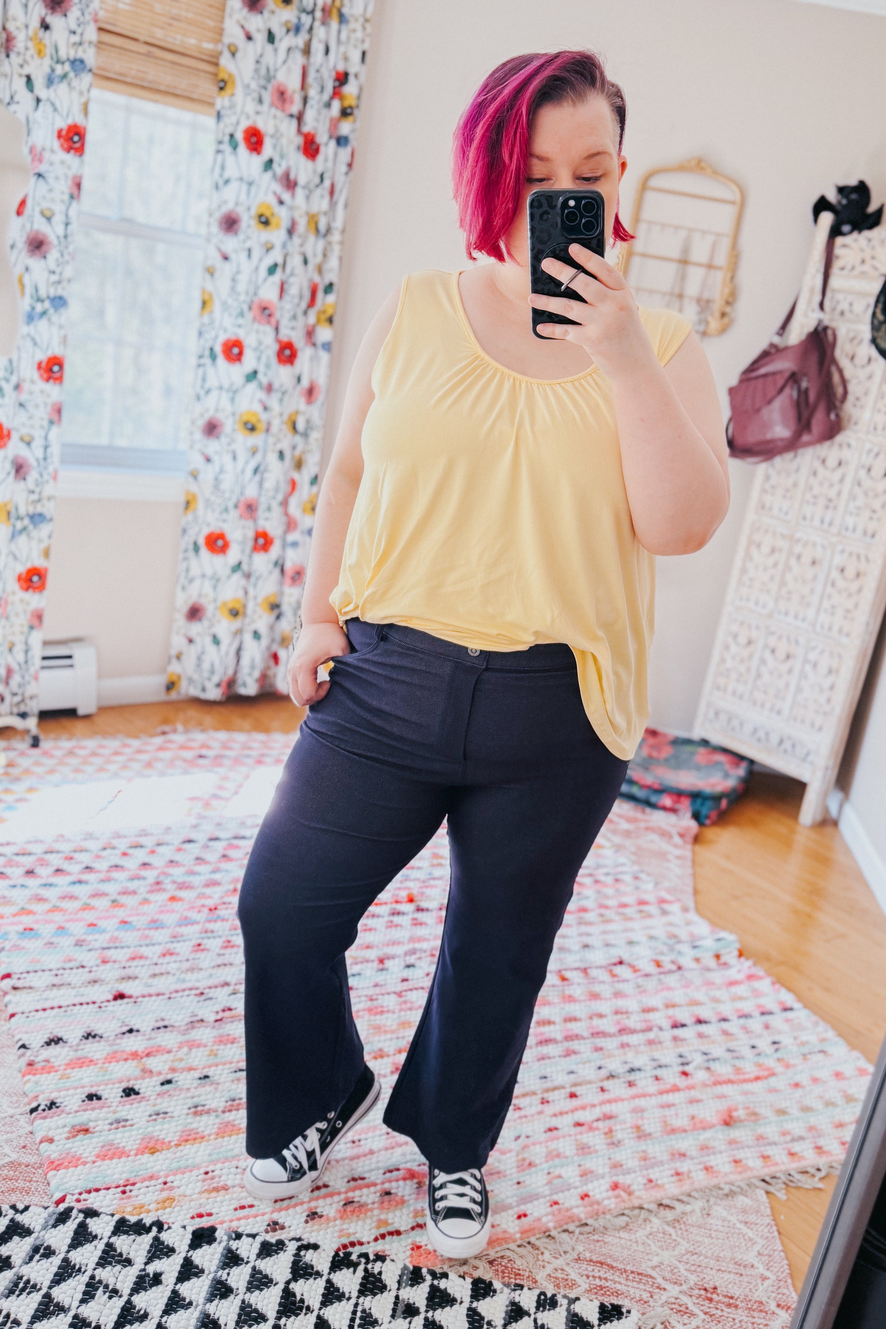 Woman with short pink hair wearing sleeveless yellow top and Classic Charm Cropped Pants taking mirror selfie indoors