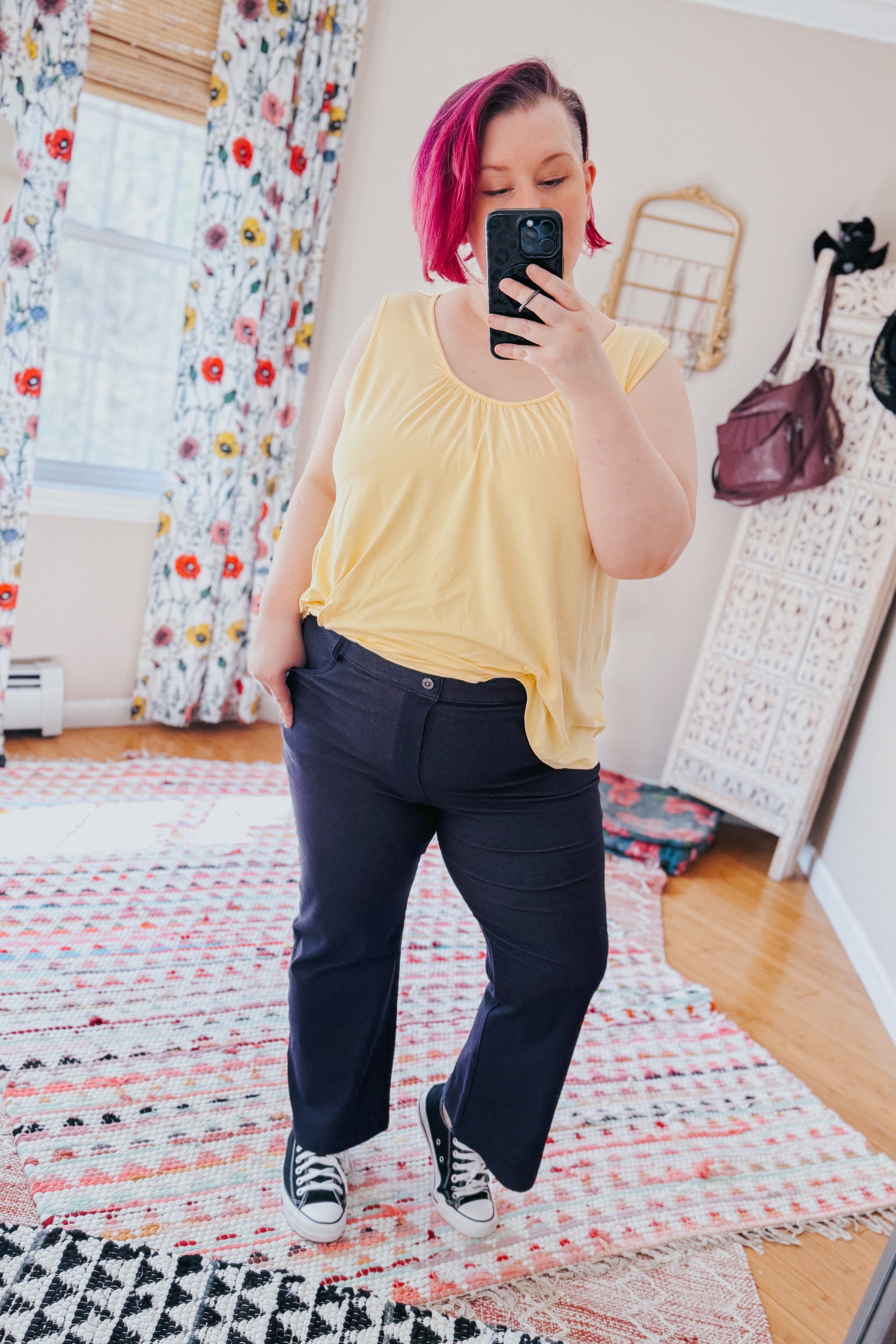 Woman with short pink hair wearing sleeveless yellow top and Classic Charm Cropped Pants taking selfie in bright room
