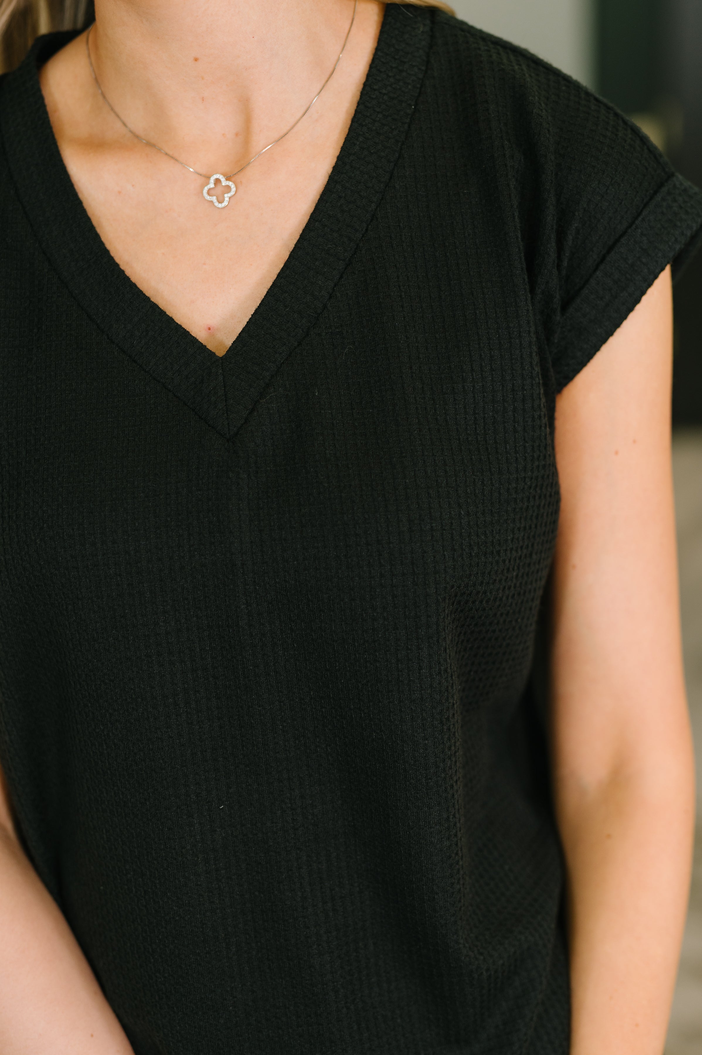 Close-up of woman wearing black textured V-neck tee with short sleeves and delicate silver necklace indoors