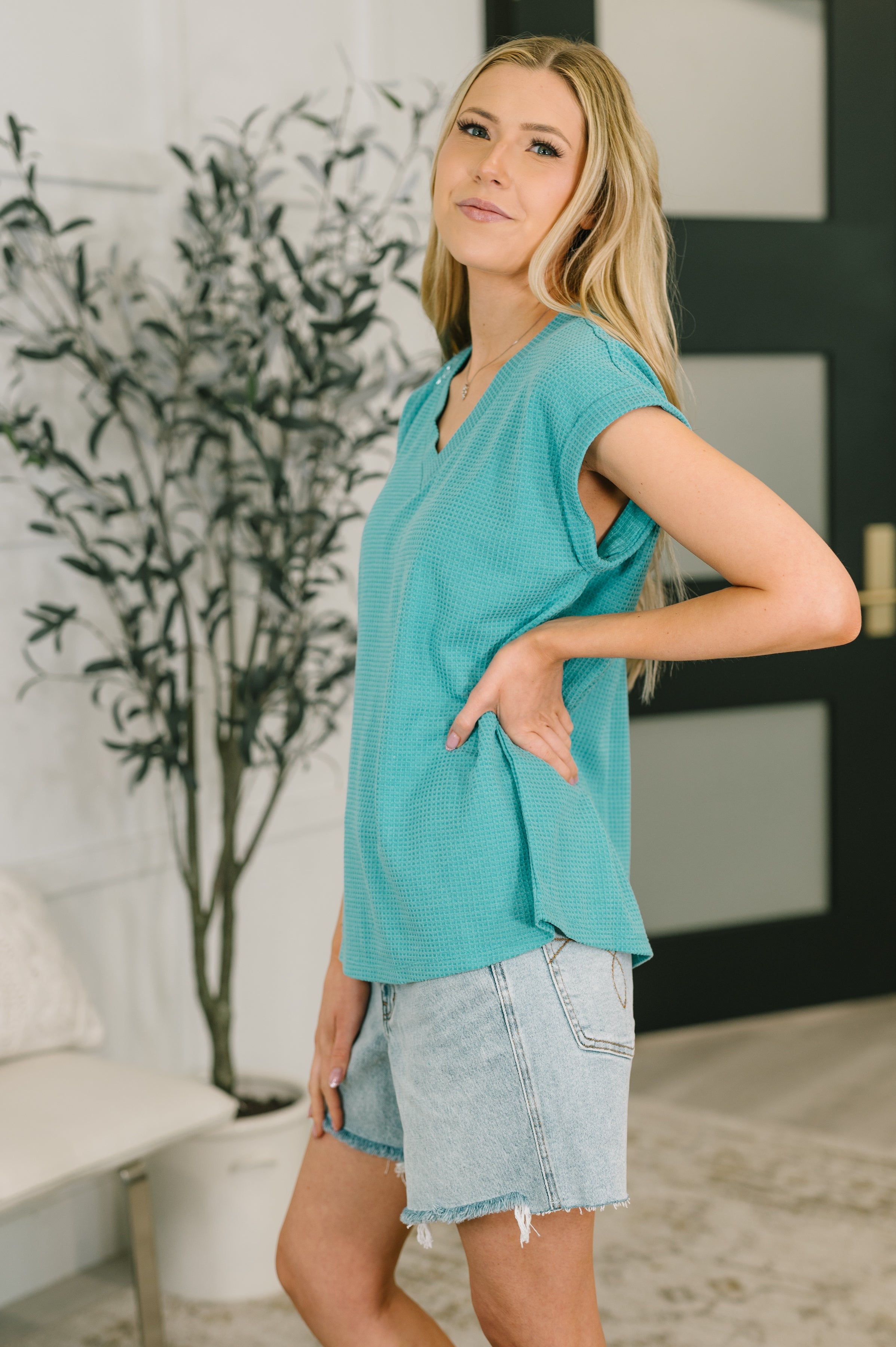 Woman wearing teal textured relaxed V-neck tee with rolled sleeves paired with light wash denim shorts indoors
