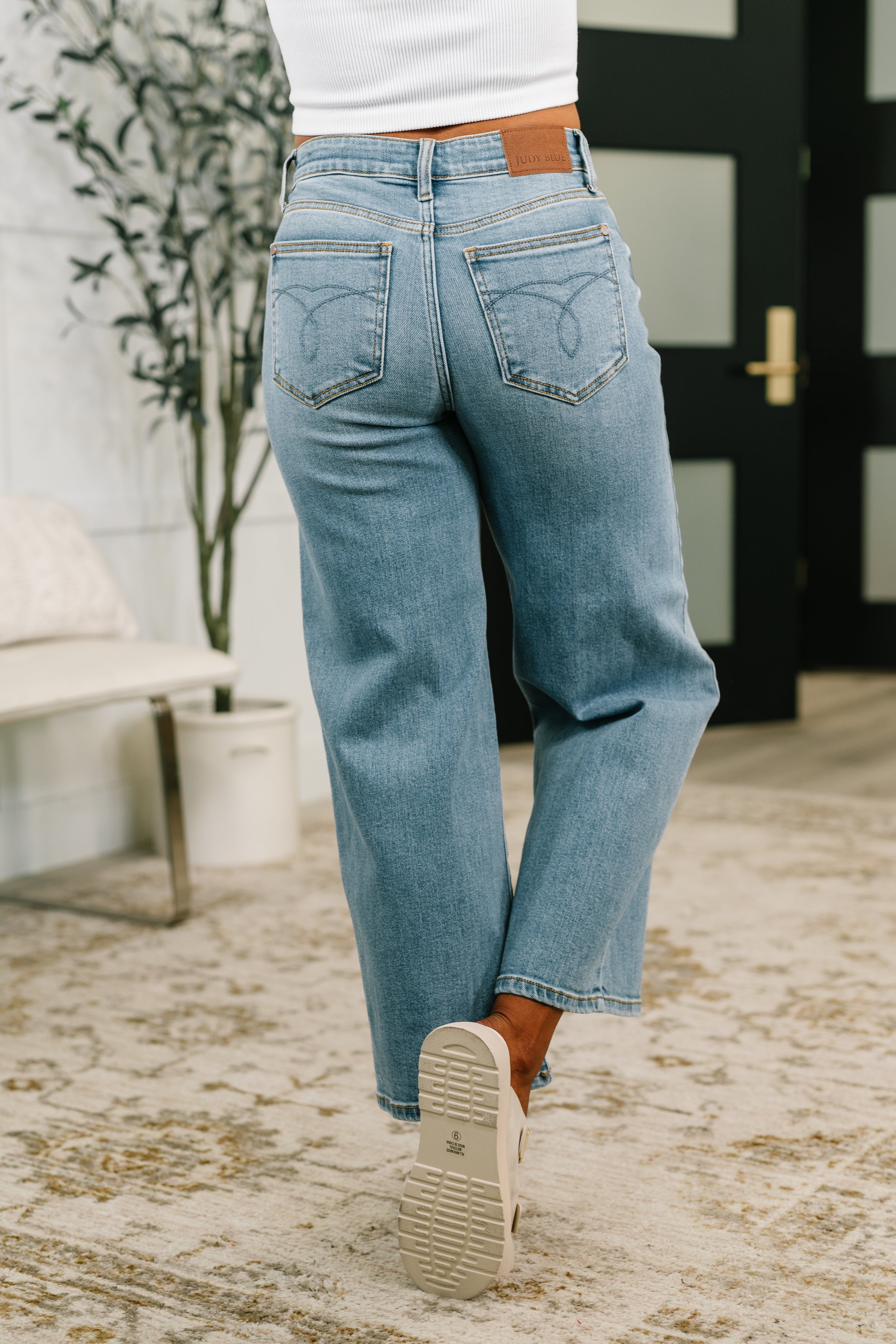 Rear view of mid-rise blue wide leg jeans with ankle length worn indoors by person in white top