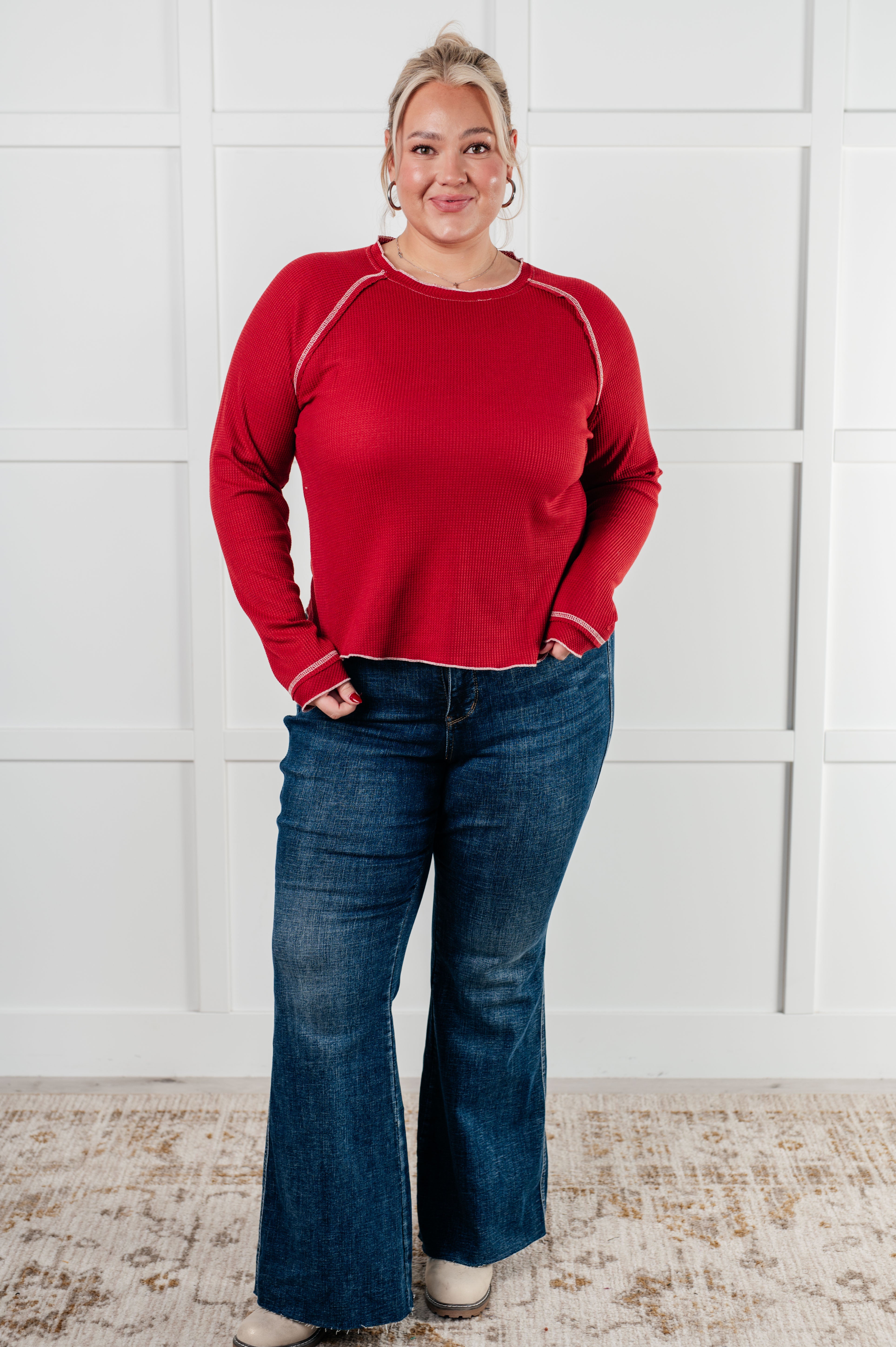 Smiling plus-size woman wearing red Clever Expression Long Sleeve Top with contrast stitching and dark flare jeans indoors